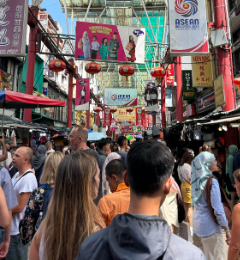 Mercado callejero abarrotado con arcos rojos, faroles y letreros; gente caminando y comprando en el sudeste asiático.