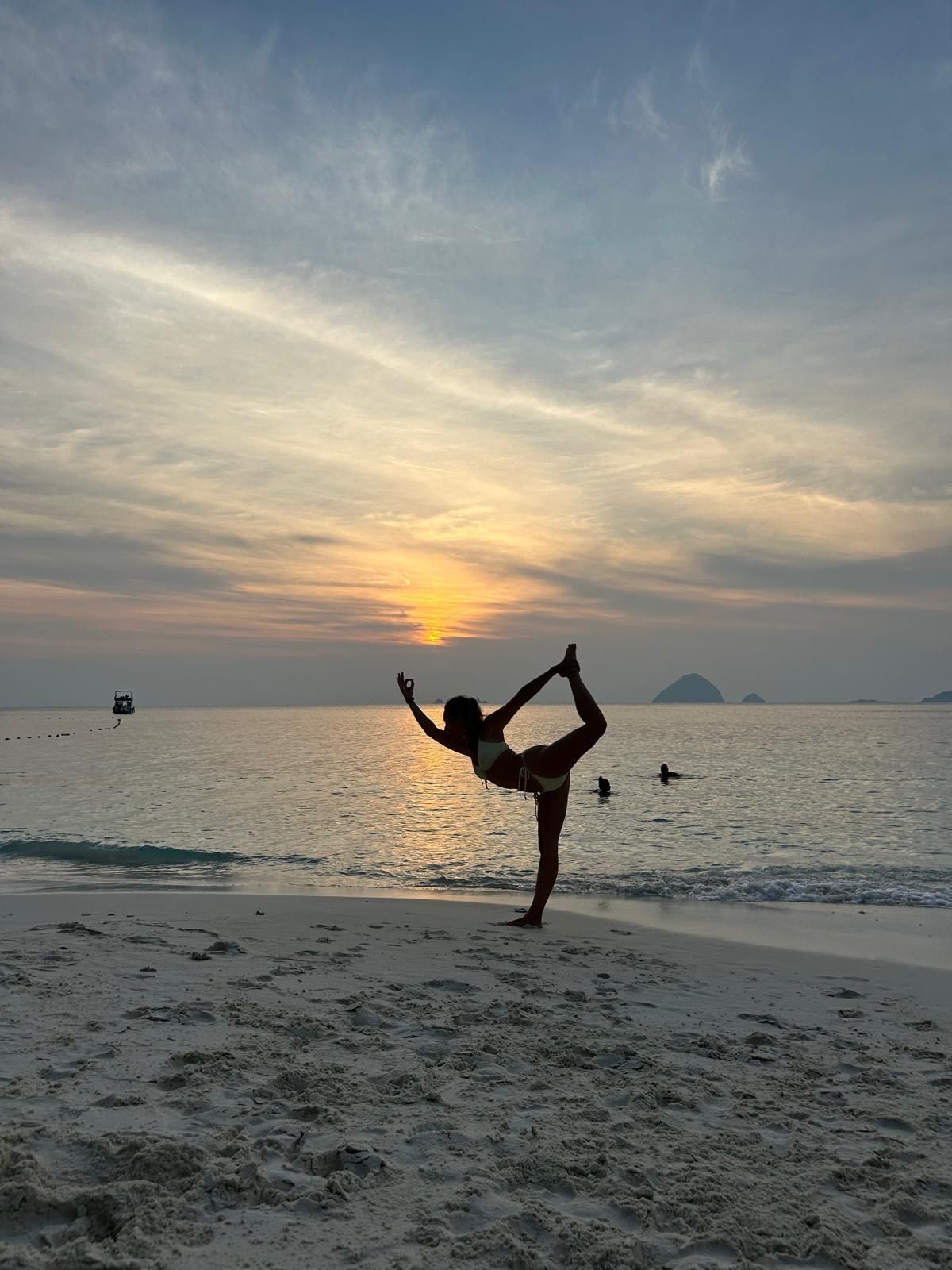 Persona en postura de yoga en la playa al atardecer, con el océano y el cielo de fondo.