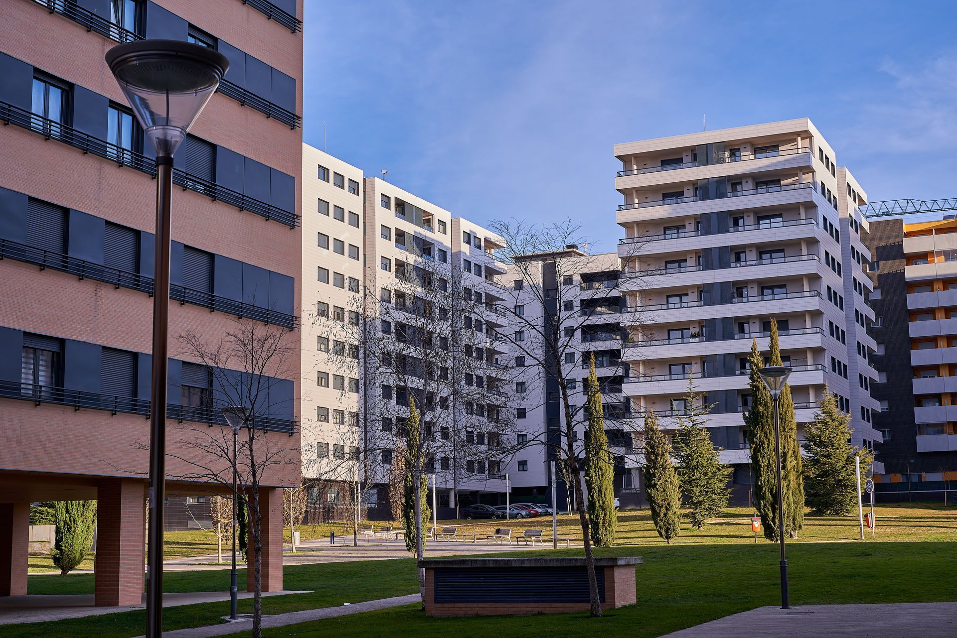 Modernos edificios de apartamentos con balcones y un espacio verde central bajo un cielo azul.