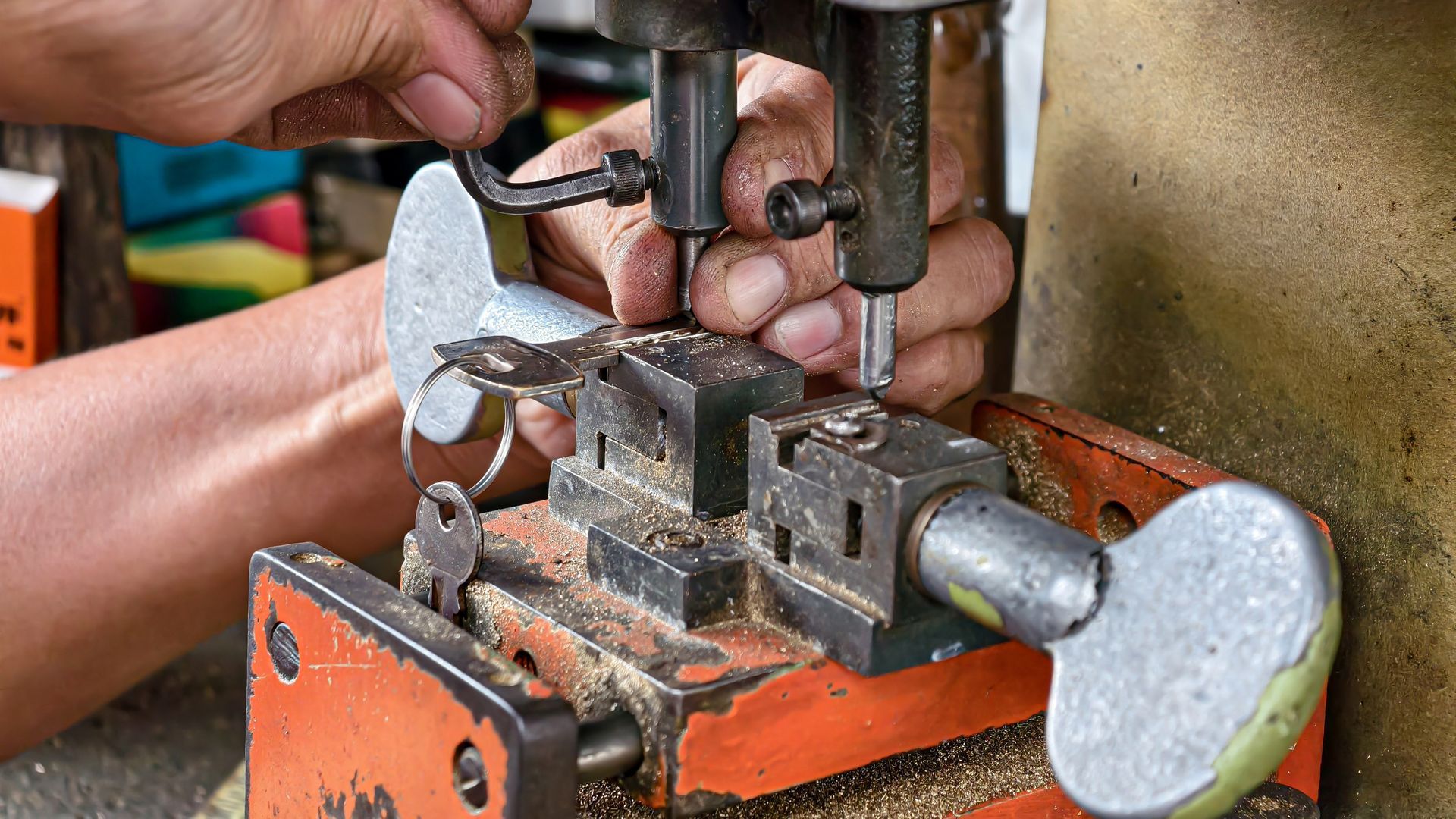 Une personne utilise une machine à tailler les clés pour reproduire une clé métallique, celle-ci étant maintenue fermement dans l'étau de la machine.
