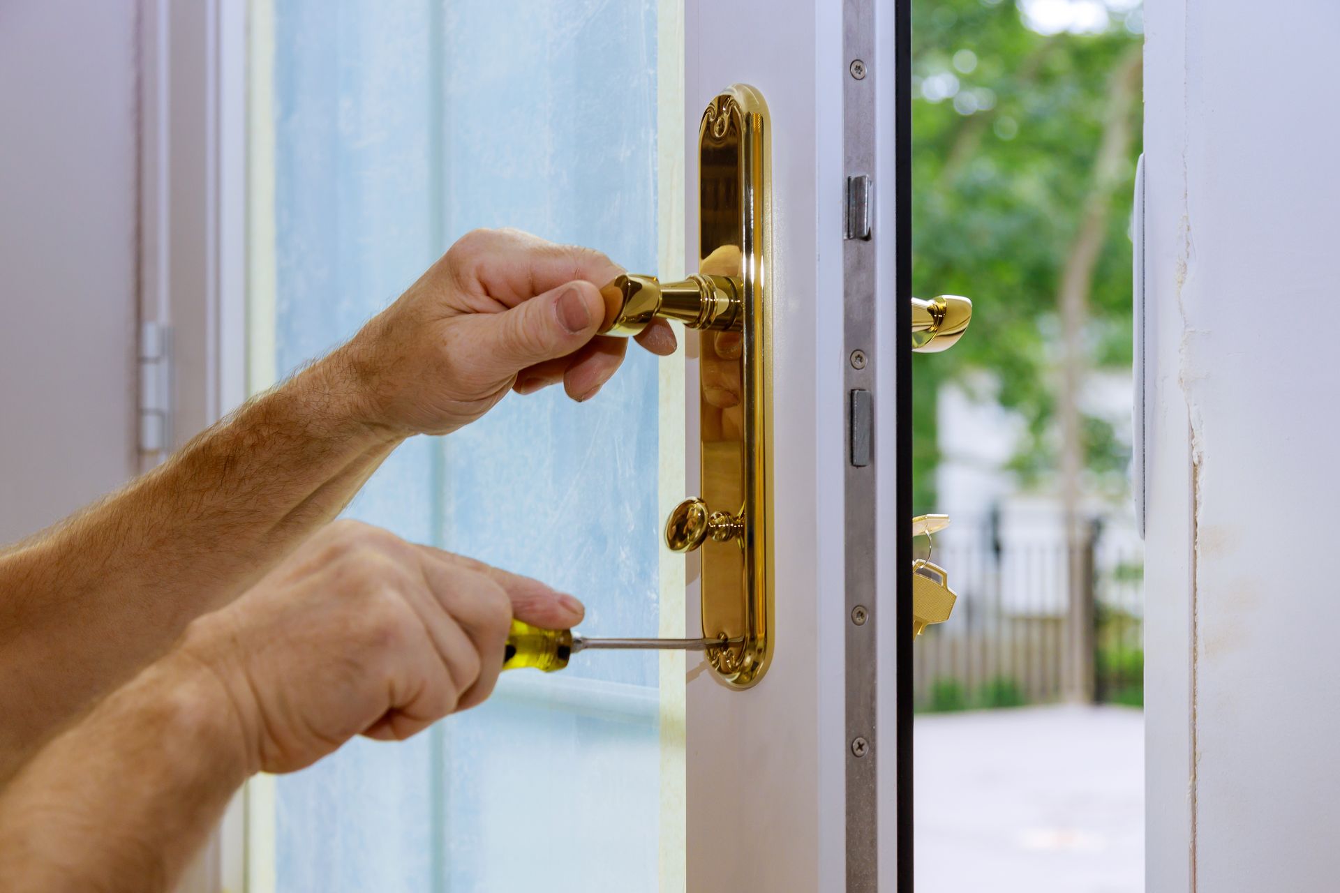 Gros plan sur des mains utilisant un tournevis pour installer une poignée de porte en laiton sur une porte blanche.