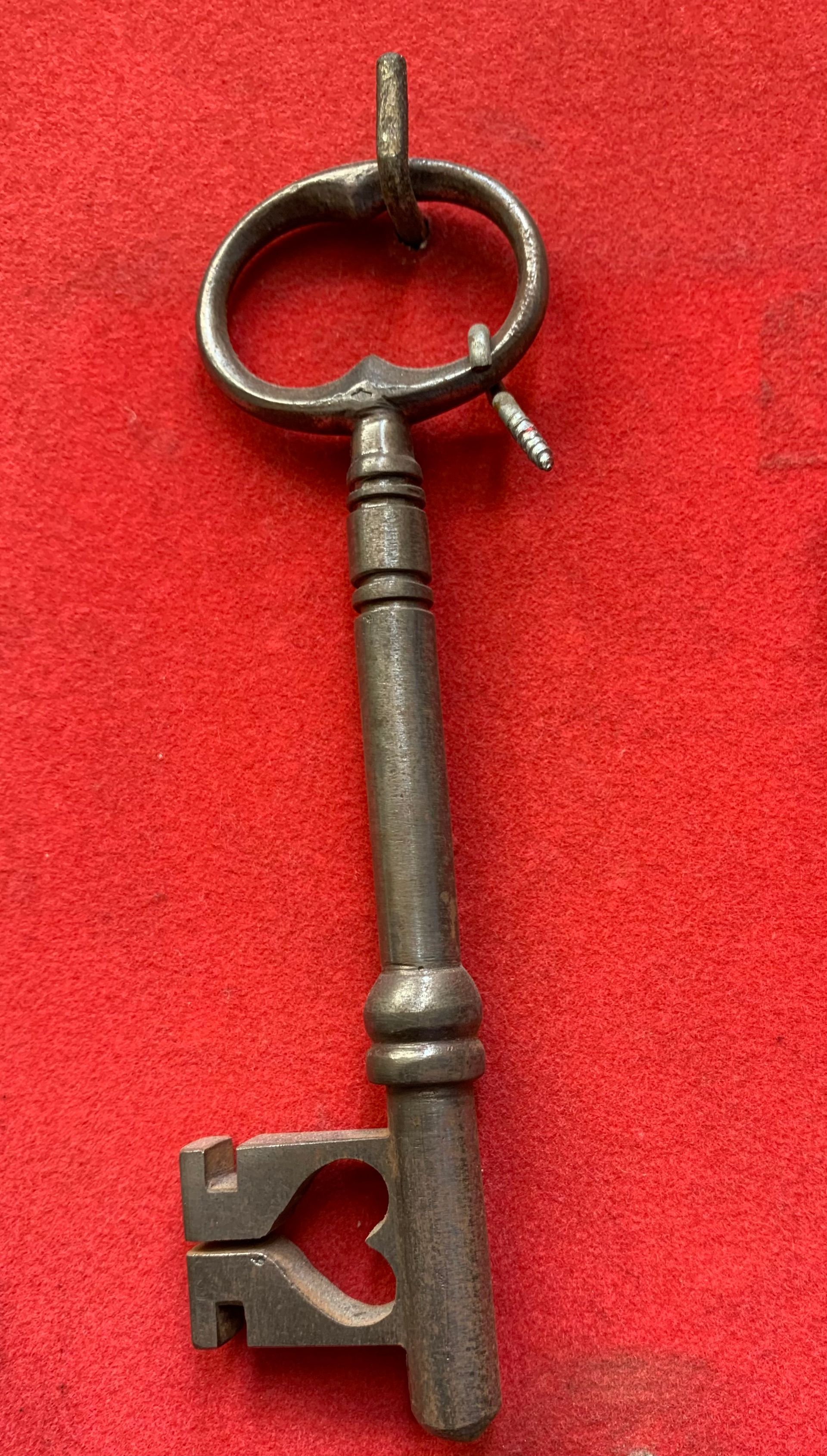 Une clé en métal ancienne et ornée, avec une découpe en forme de cœur dans son poinçon, présentée sur un fond rouge texturé éclatant.