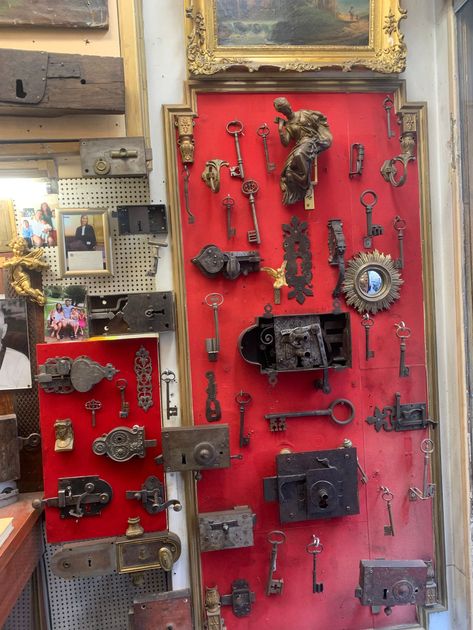 Une collection éclectique de clés anciennes, de serrures, de sculptures en métal et de petites photographies encadrées, exposée sur un mur en bois.