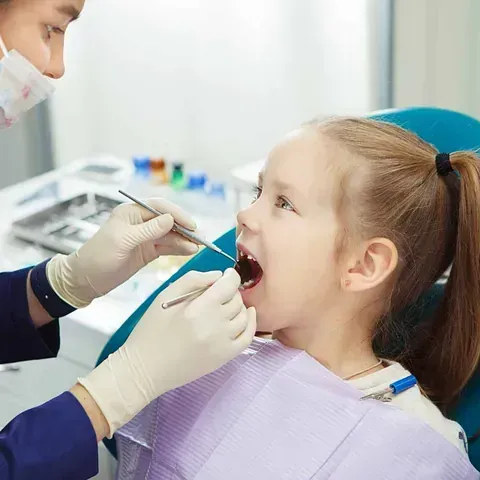 A una niña le están examinando los dientes un dentista.