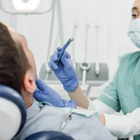 Un hombre está sentado en una silla dental mientras un dentista examina sus dientes.