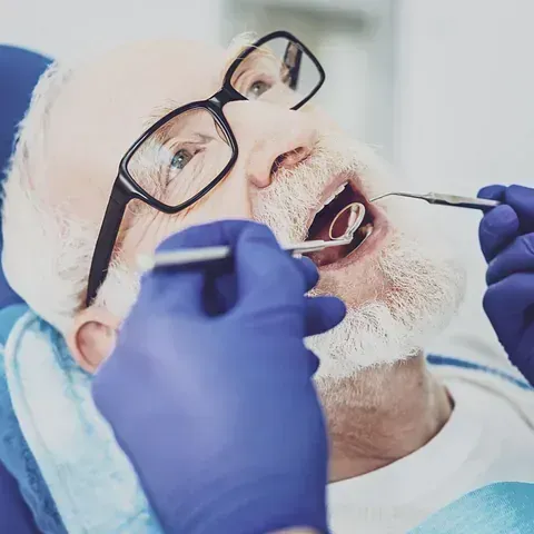 Un hombre con gafas se hace examinar los dientes por un dentista.