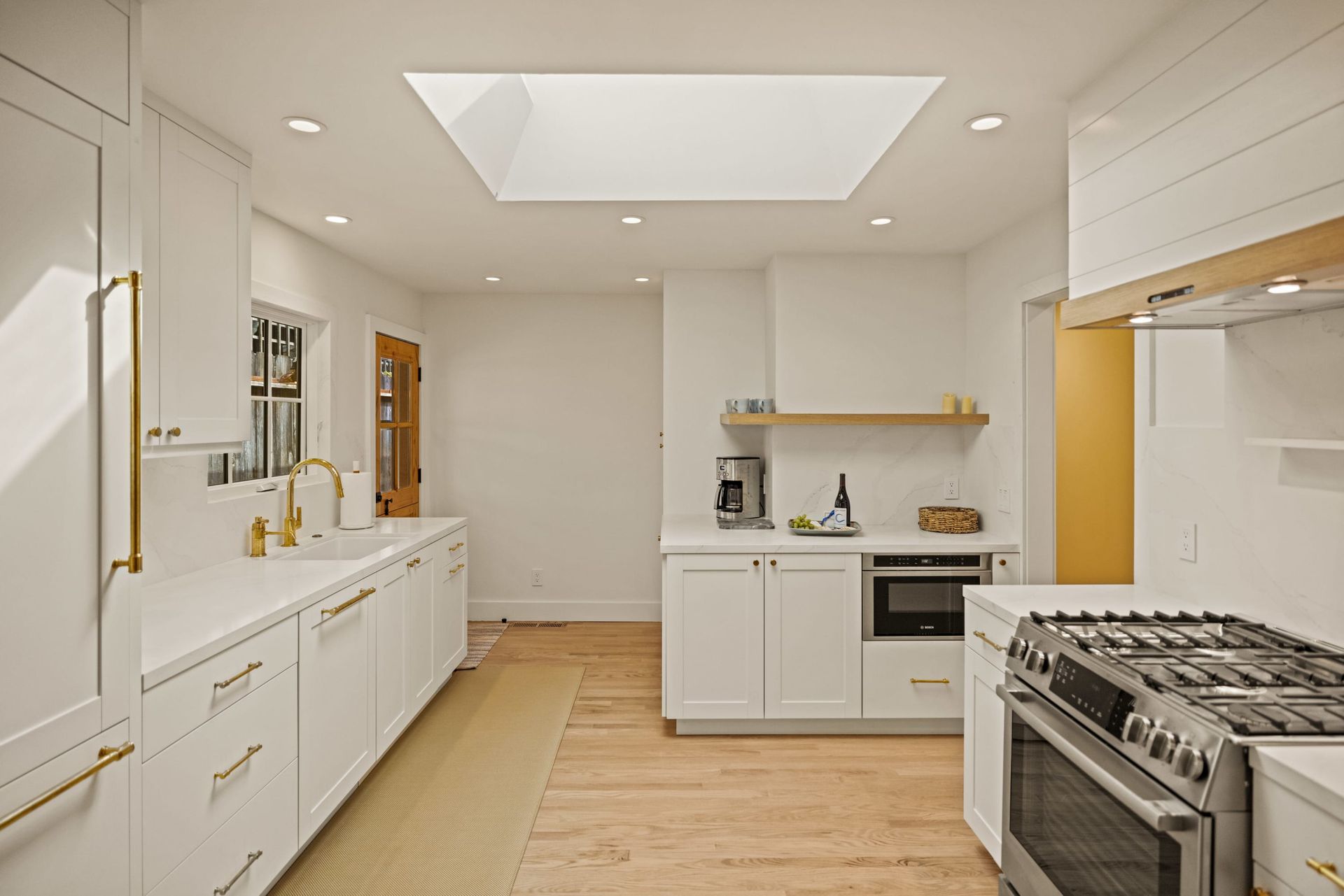A kitchen with white cabinets , a stove , and a skylight.