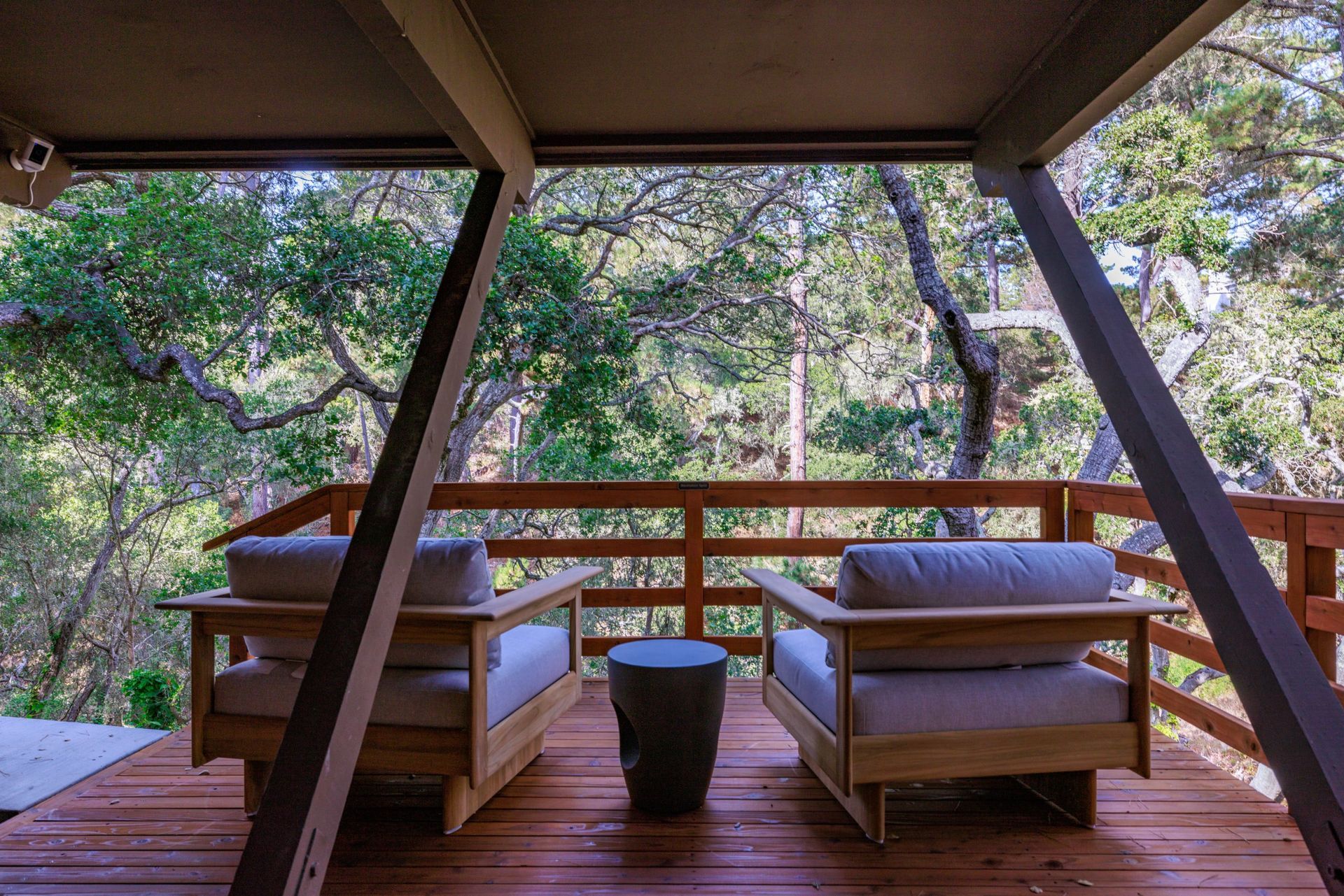 Two chairs are sitting on a wooden deck with trees in the background.