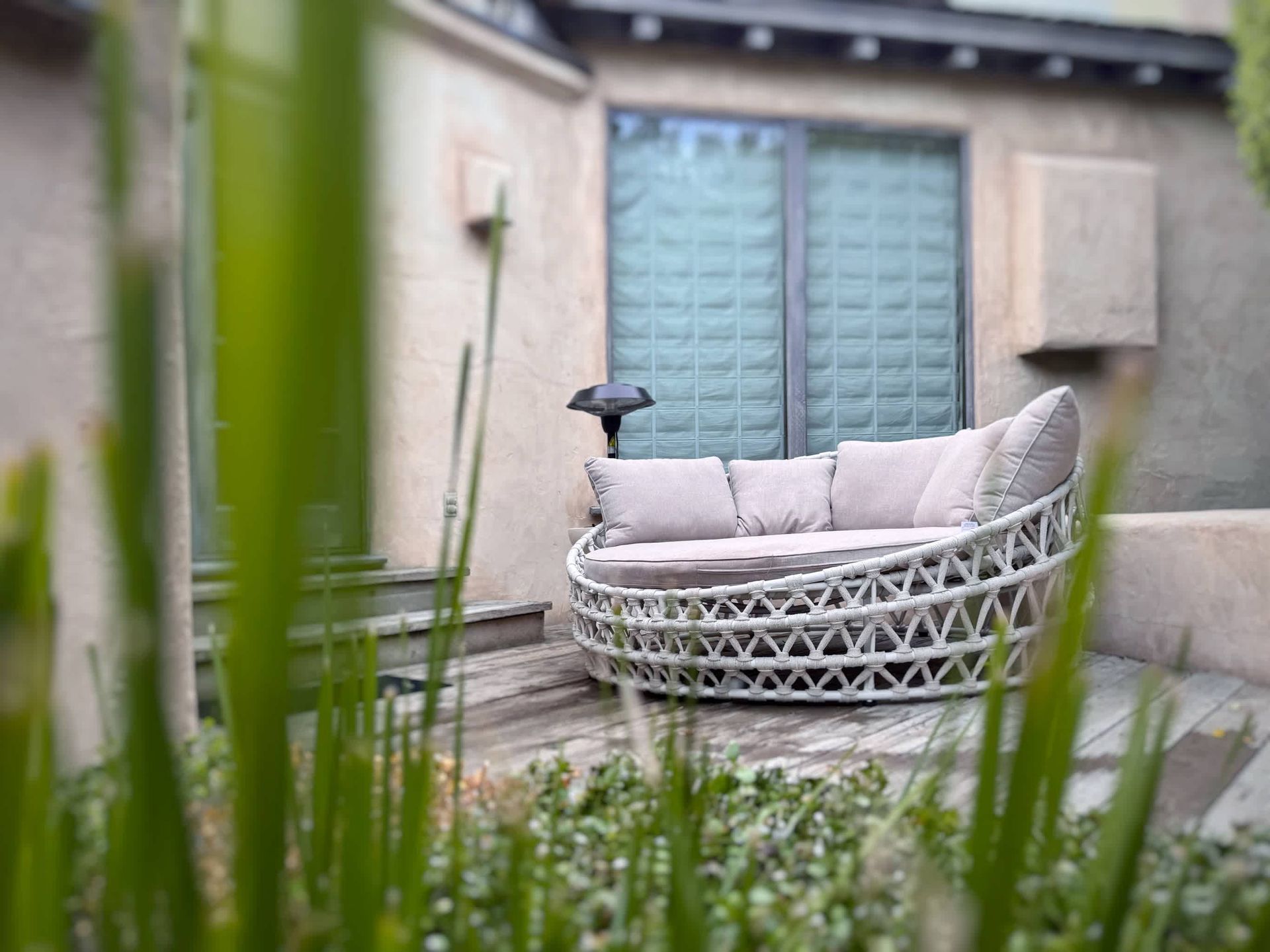 A round couch is sitting on a patio next to a window.