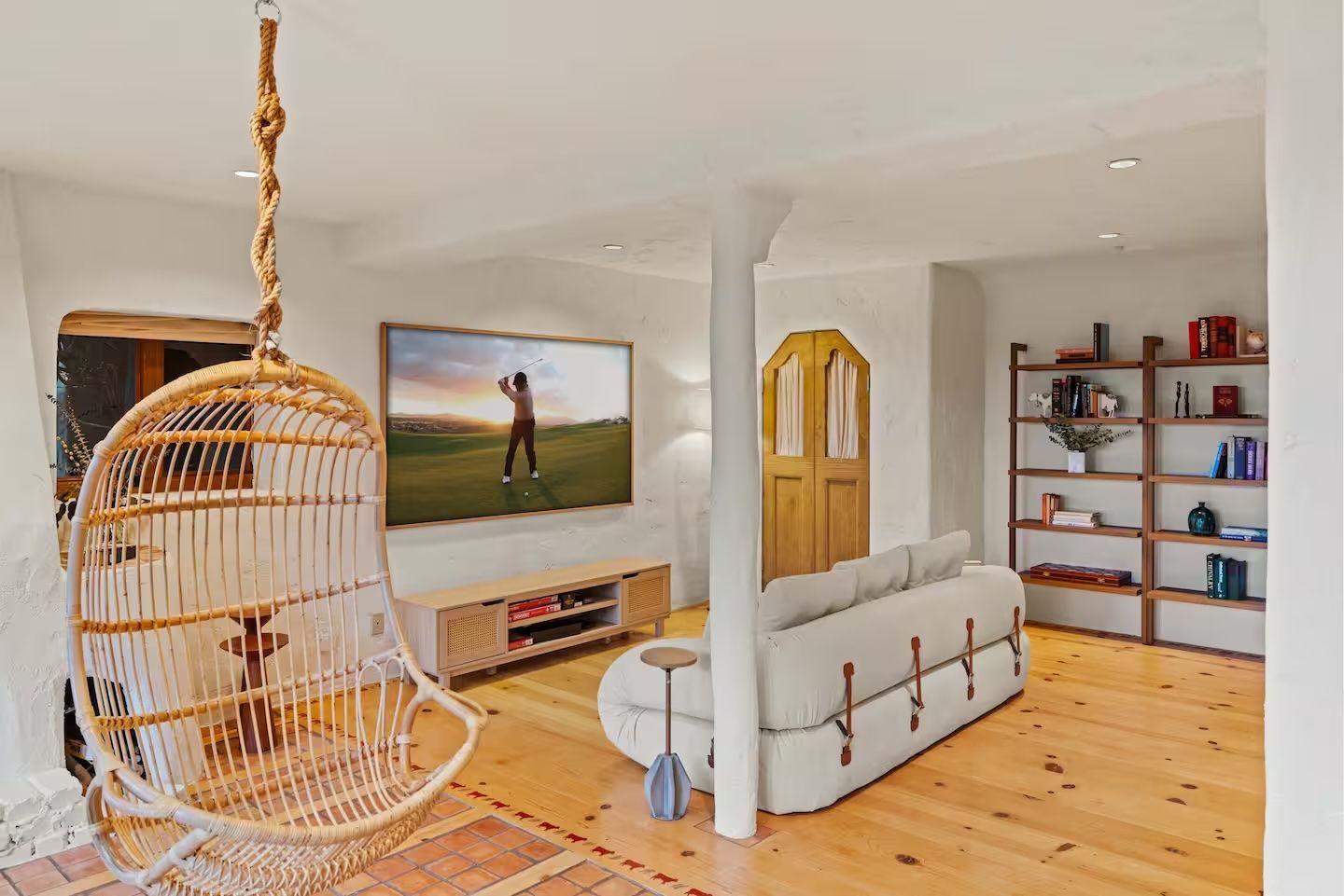 A living room with a wicker chair hanging from the ceiling and a couch.