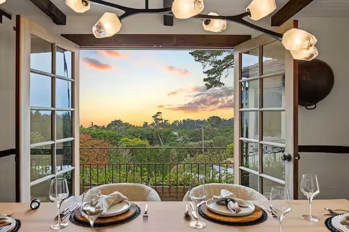 A dining room table with plates , glasses , and a view of the sunset.