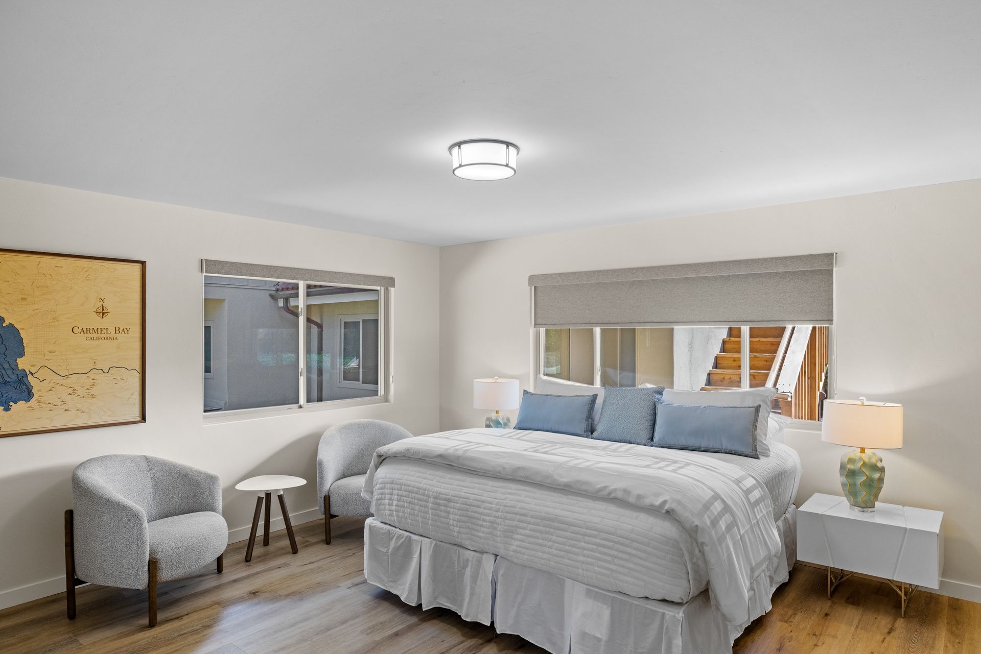 A bedroom with a king size bed , two chairs , a nightstand and a large window.