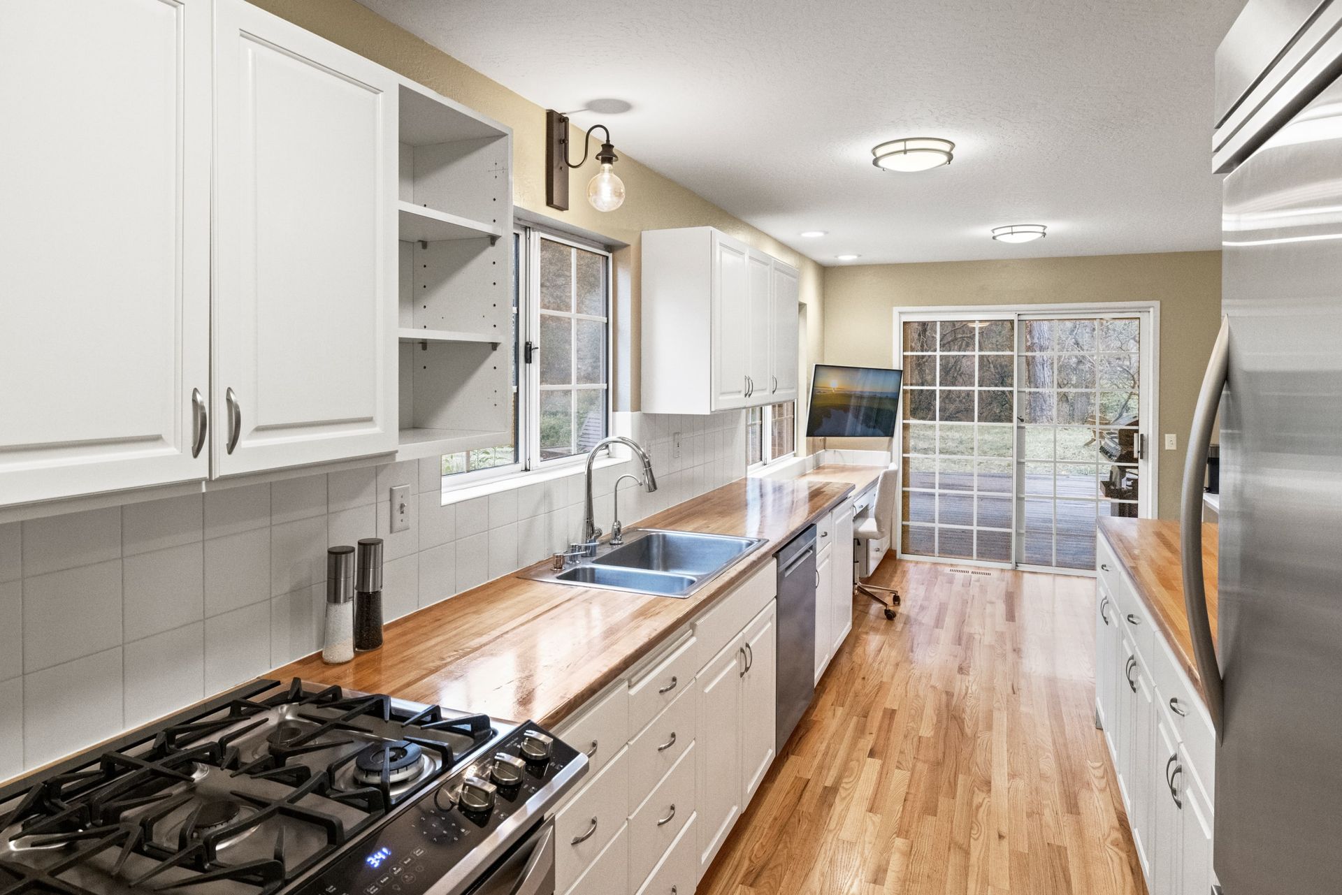 A kitchen with white cabinets , stainless steel appliances , hardwood floors and a stove.