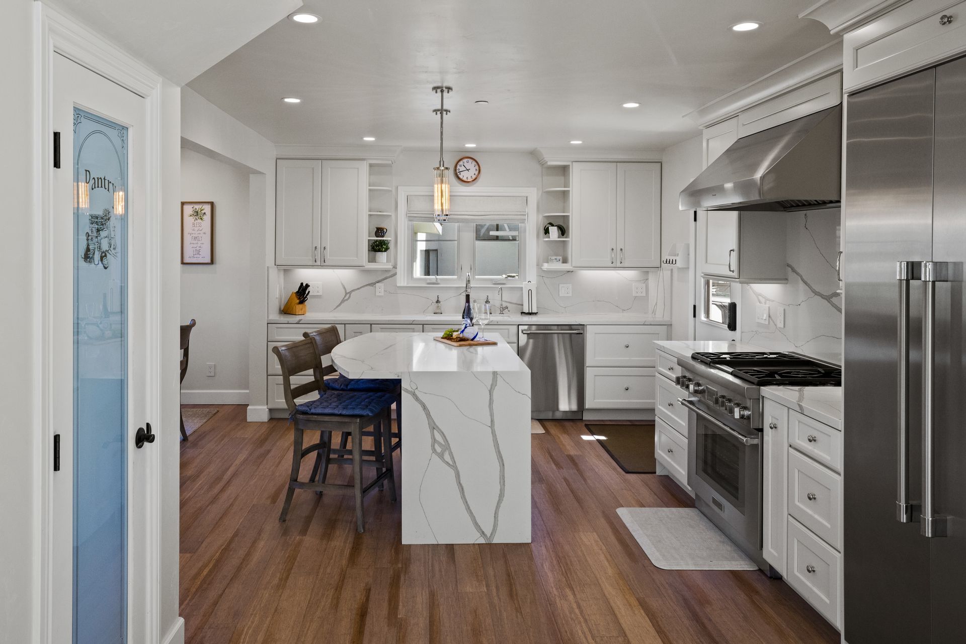 A kitchen with white cabinets , stainless steel appliances , a large island , and hardwood floors.