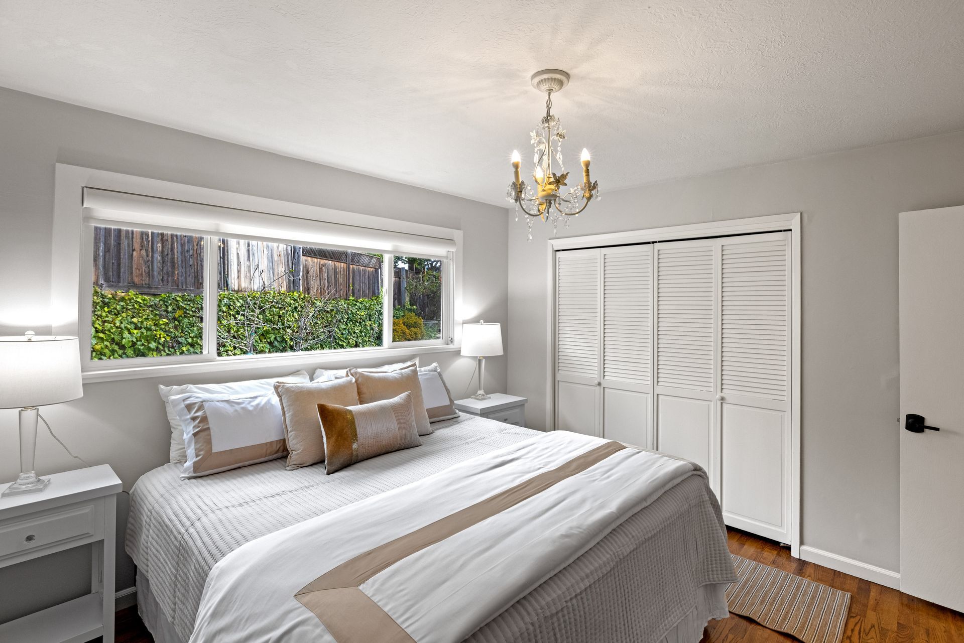 A bedroom with a bed , nightstands , a window and a chandelier.
