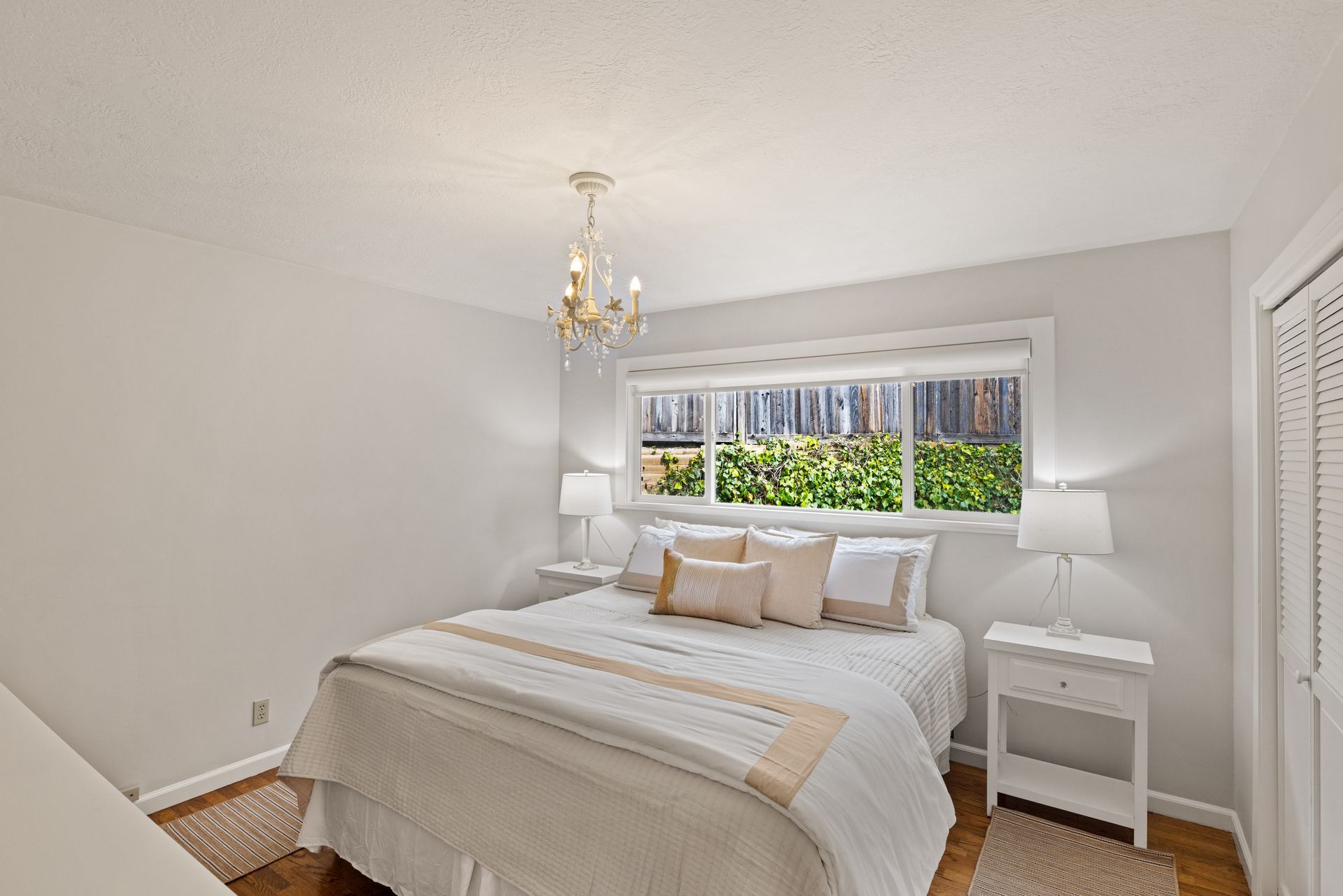 A bedroom with a king size bed , two nightstands , a window and a chandelier.