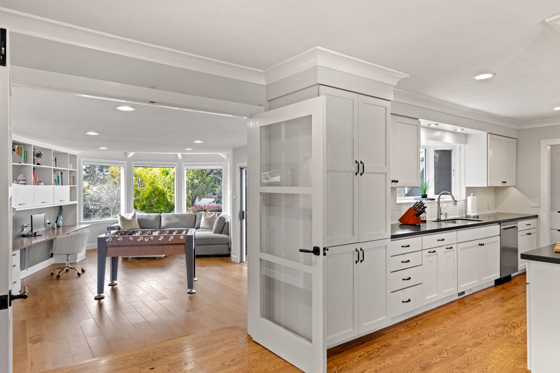 A kitchen with white cabinets and hardwood floors and a foosball table.