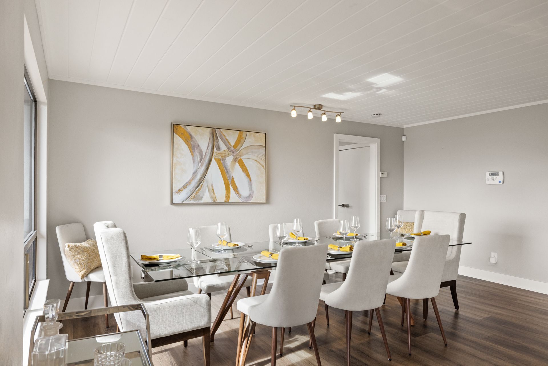 A dining room with a table and chairs and a painting on the wall.