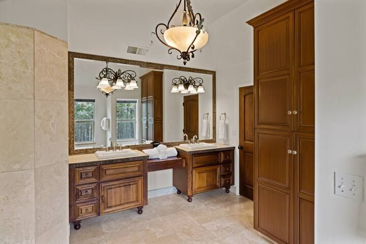 A bathroom with two sinks , two mirrors and a chandelier.
