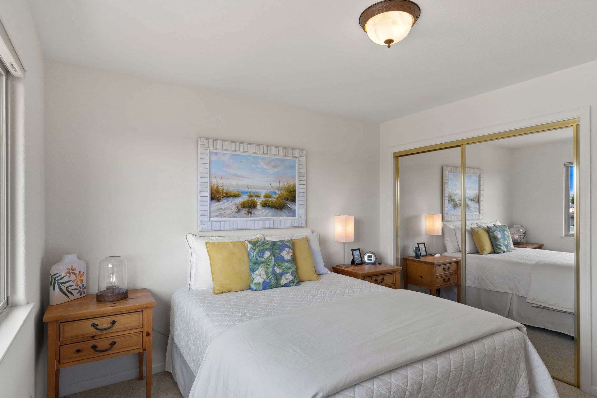 A bedroom with a bed , two nightstands , a mirror and a painting on the wall.