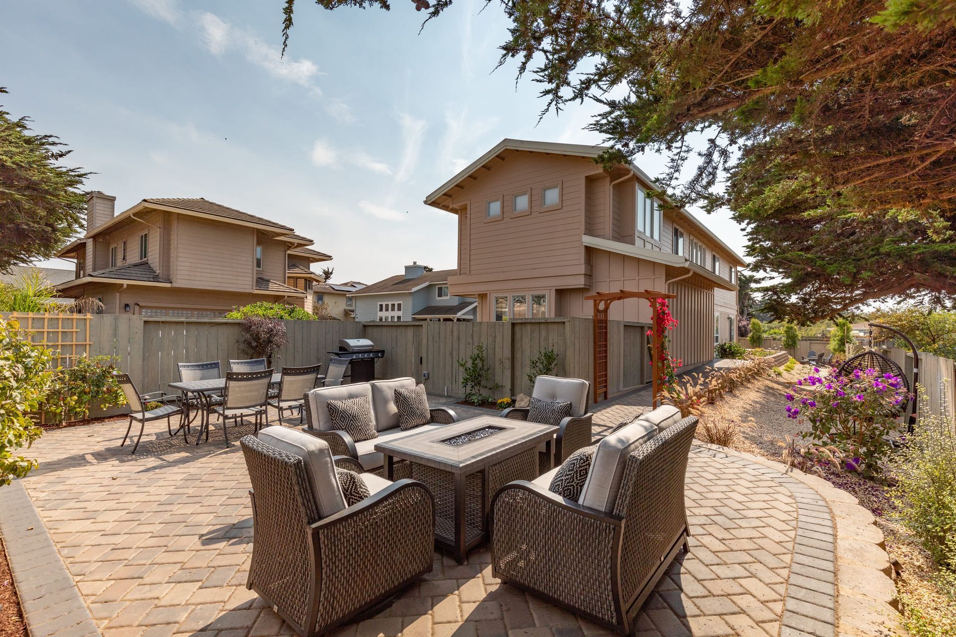 A patio with wicker furniture and a fire pit in front of a house.