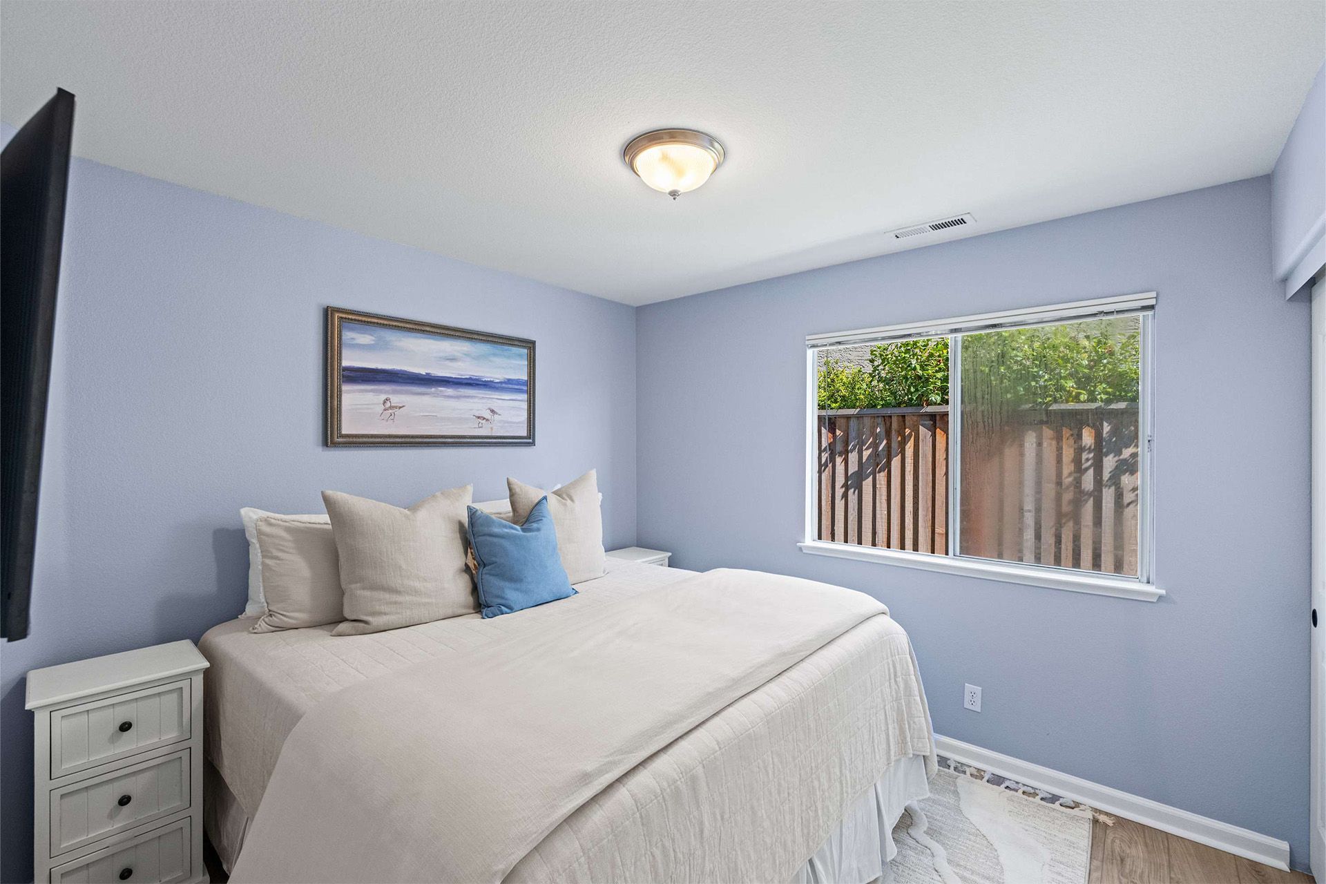 A bedroom with a bed , nightstand , television and two windows.
