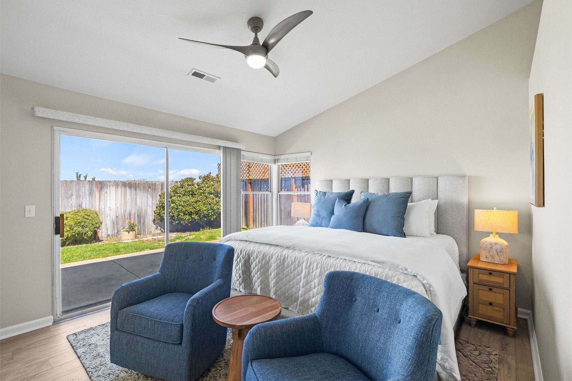 A bedroom with a king size bed , two chairs , a table and a ceiling fan.
