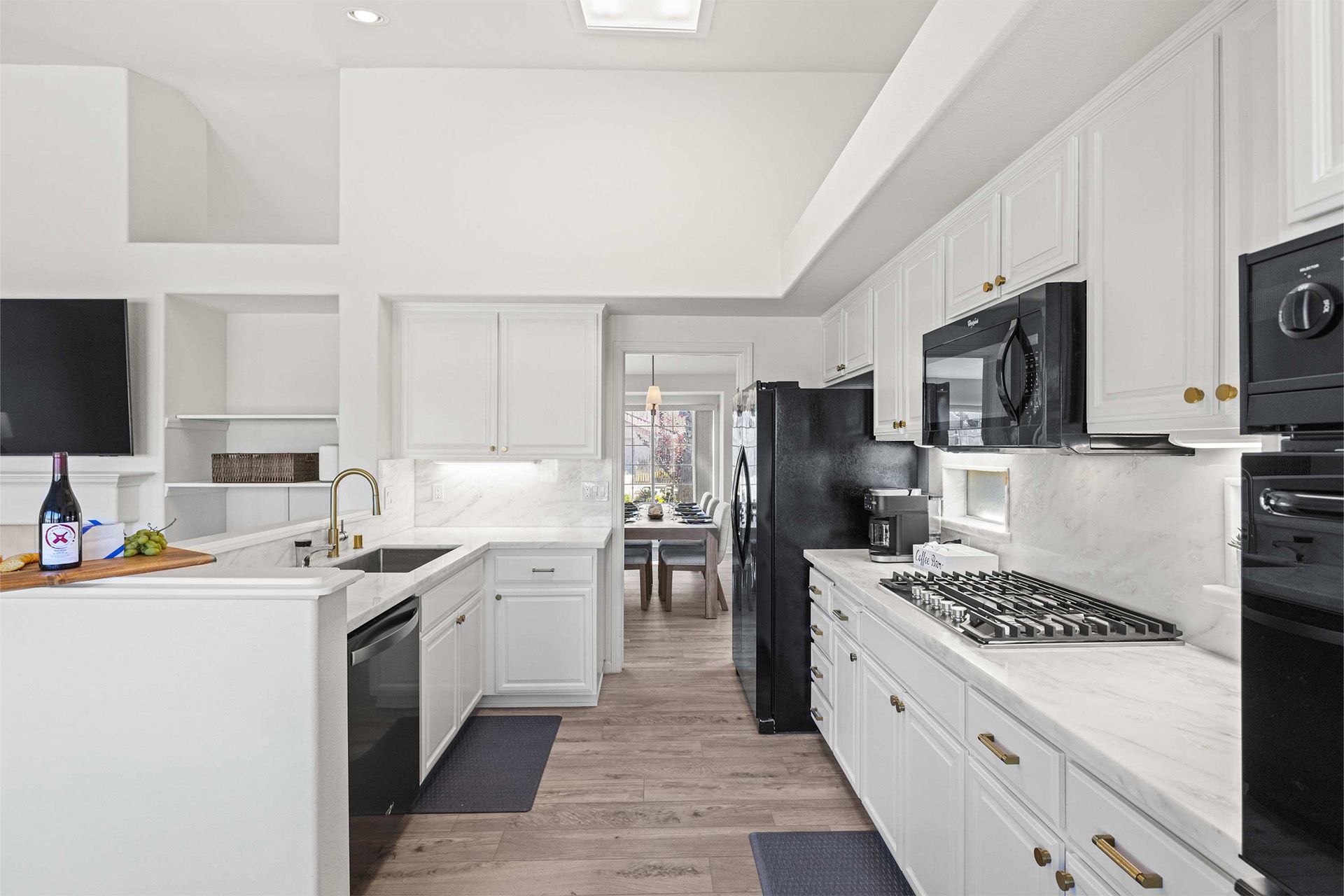 A kitchen with white cabinets and black appliances and a bottle of wine on the counter.