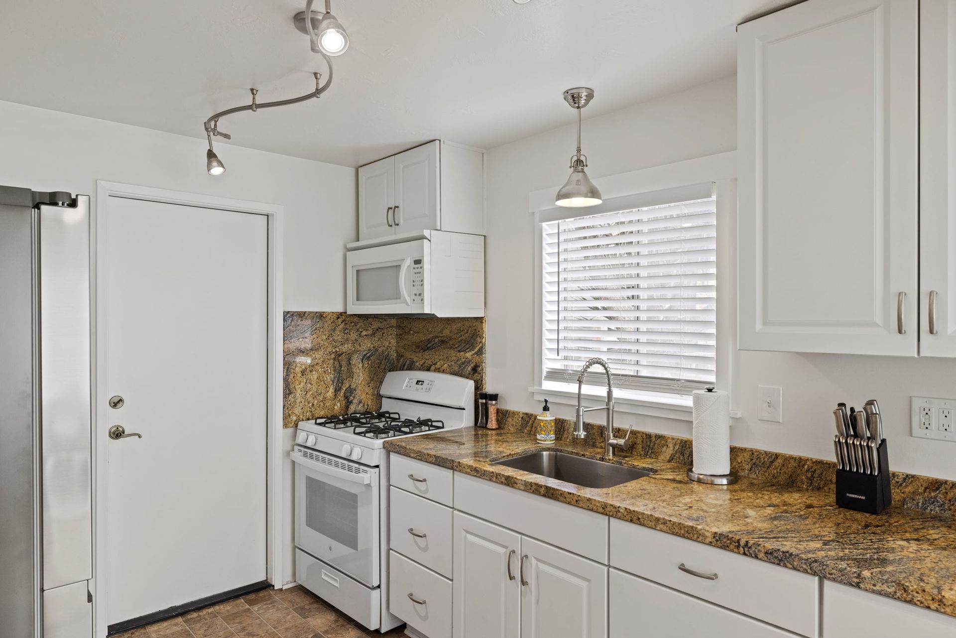 A kitchen with white cabinets , granite counter tops , a stove and a sink.