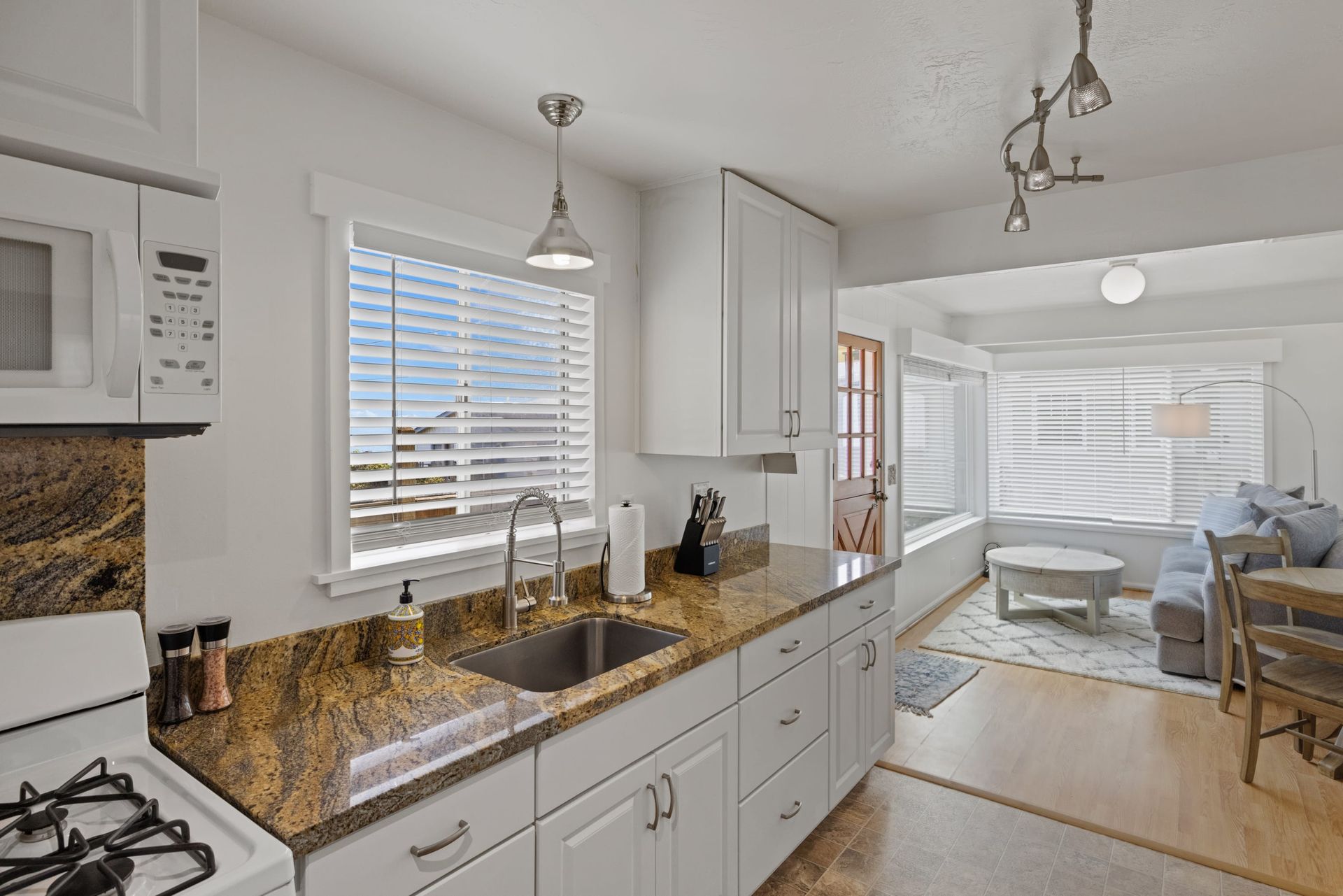 A kitchen with a sink , stove , microwave and a window.