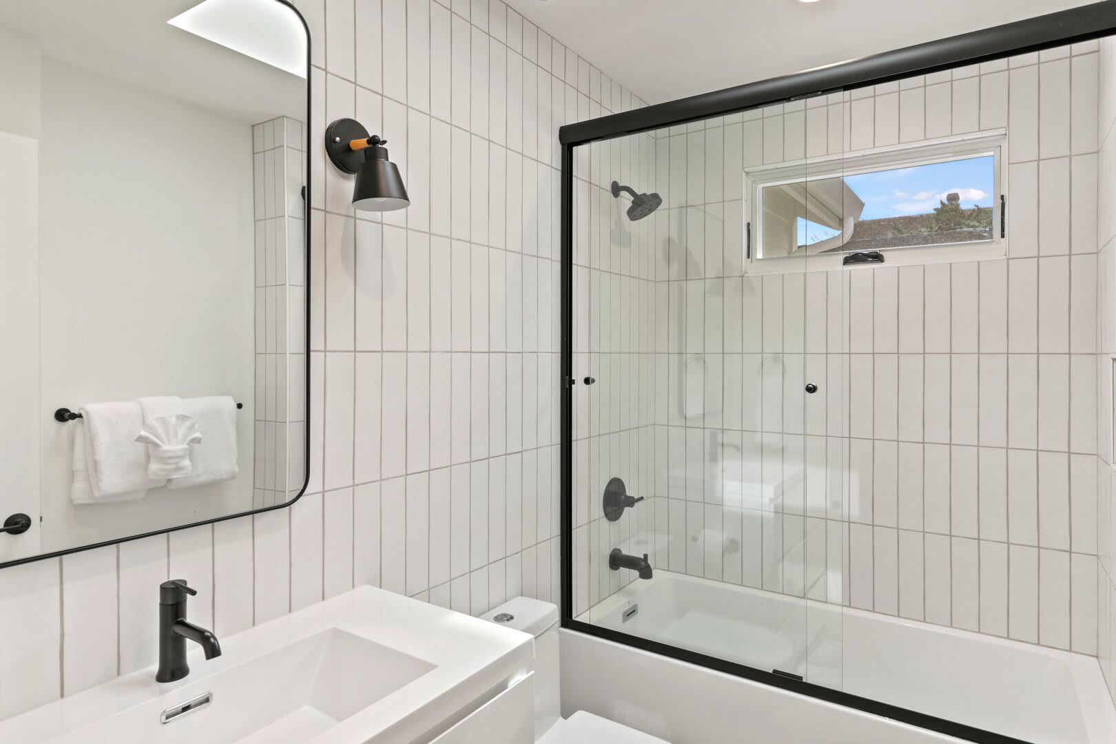 A bathroom with white tiles , a sink , a toilet , and a shower.