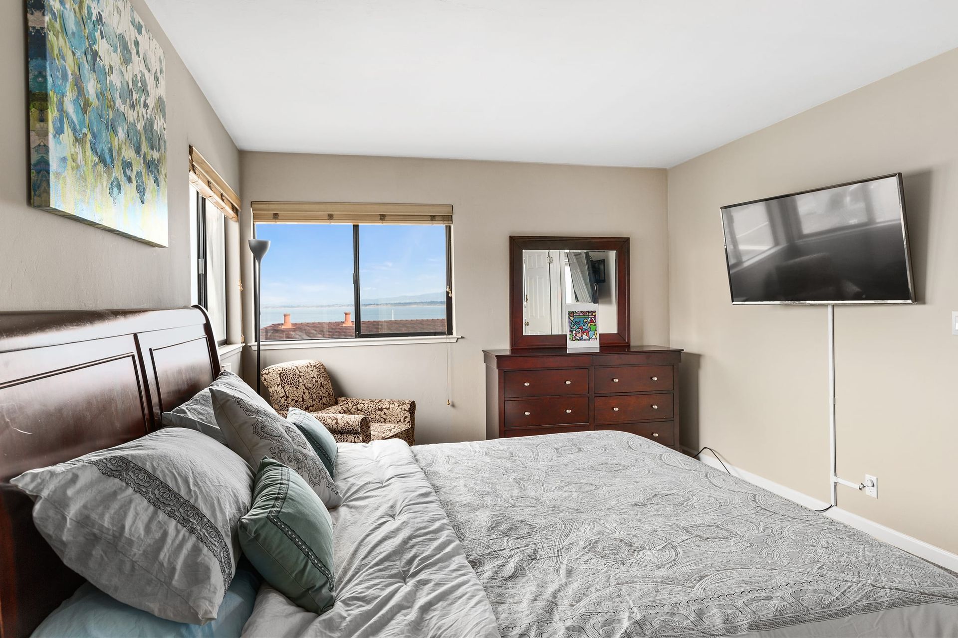 A bedroom with a king size bed , dresser , mirror and television.