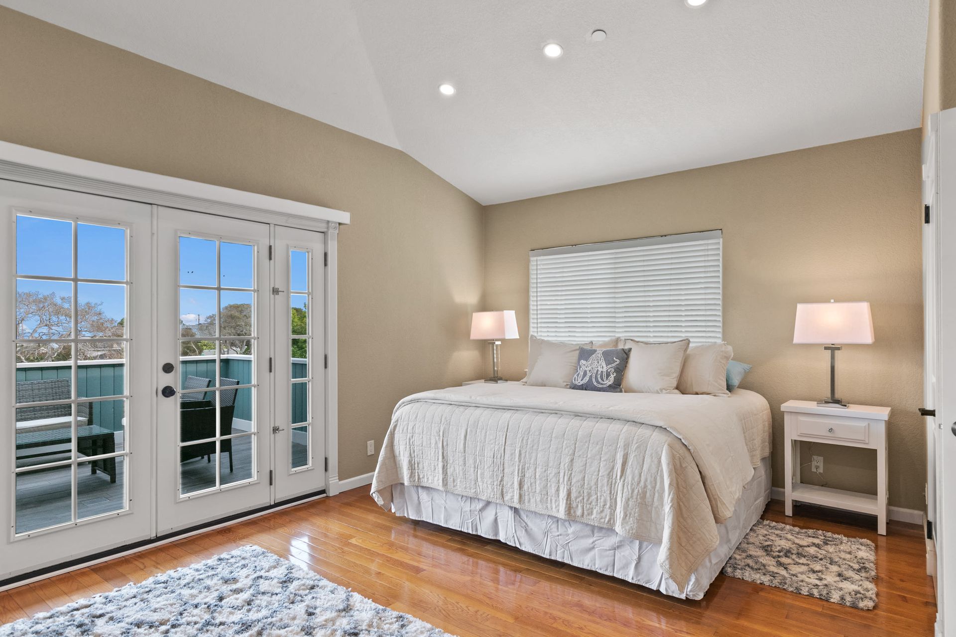 A bedroom with a king size bed , french doors , lamps and a rug.