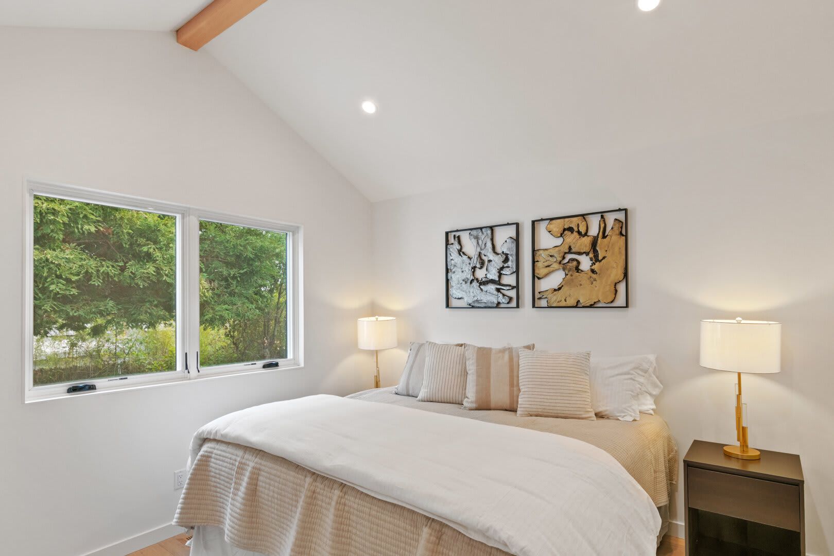 A bedroom with a bed , two lamps , and two windows.