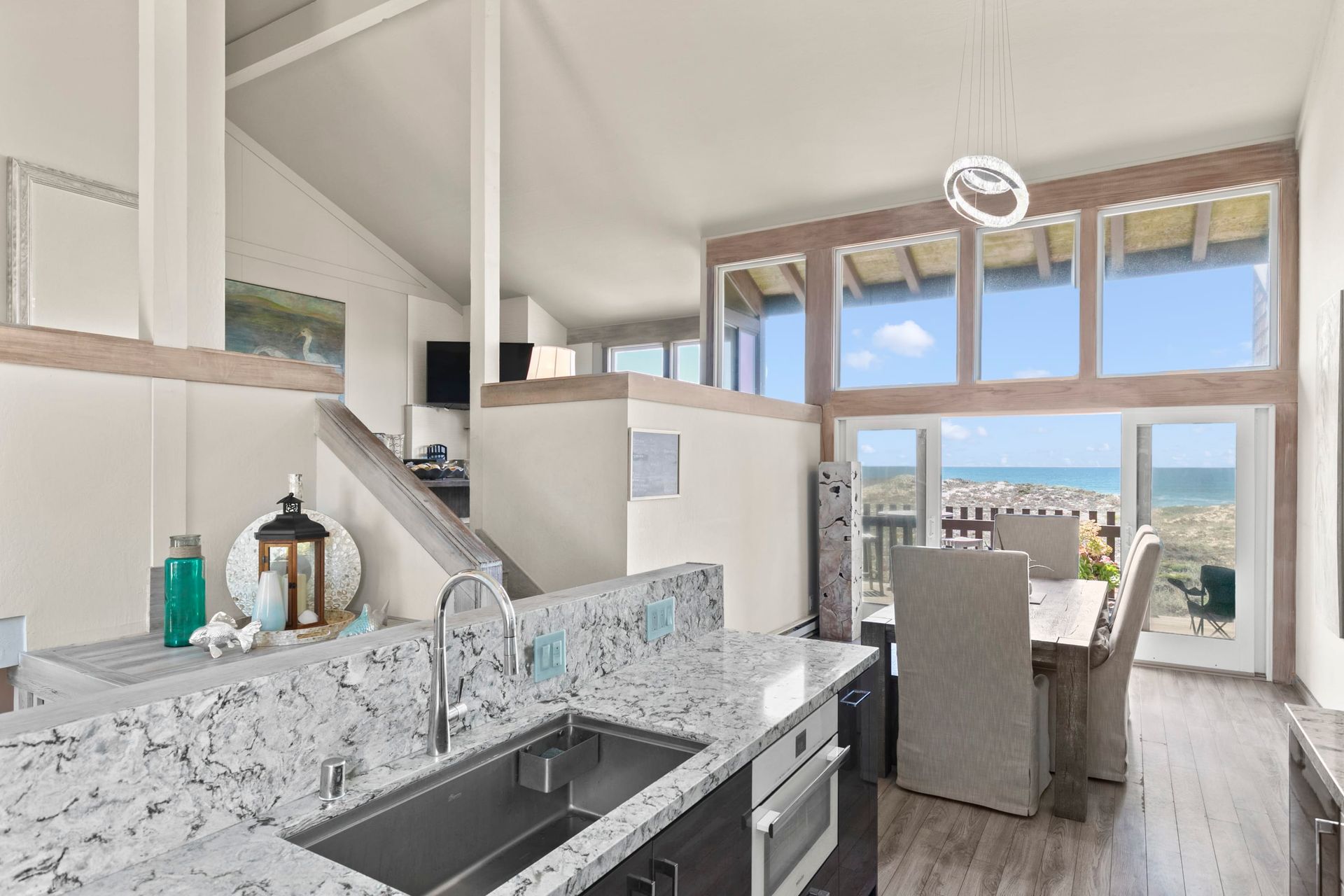 A kitchen with a sink and a dining table with a view of the ocean.