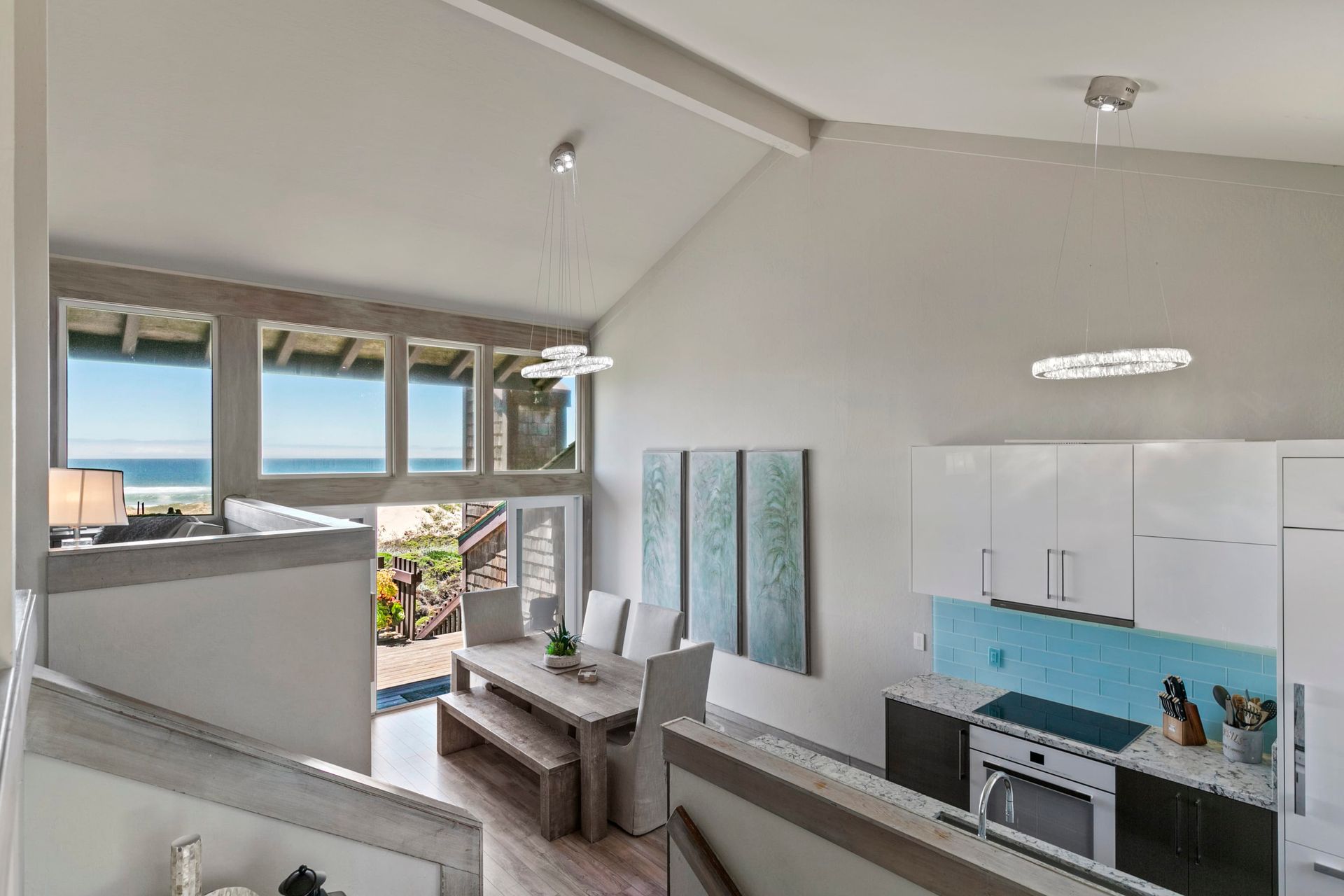 A living room with a table and chairs and a kitchen with a view of the ocean.