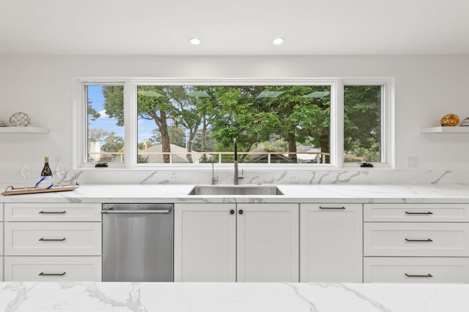 A kitchen with white cabinets , a sink , a dishwasher , and a large window.