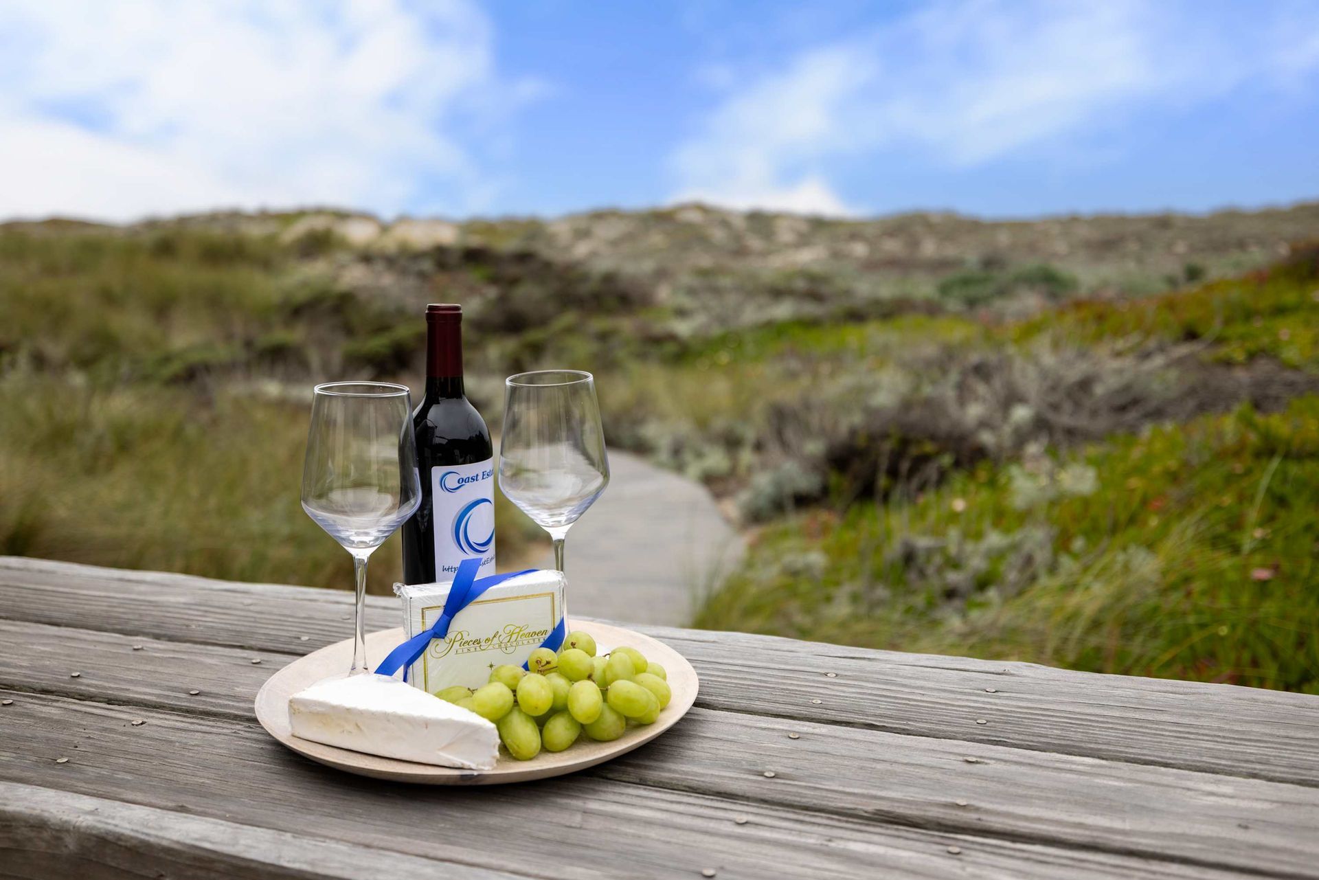 A bottle of wine , two glasses of wine , cheese and grapes on a wooden table.