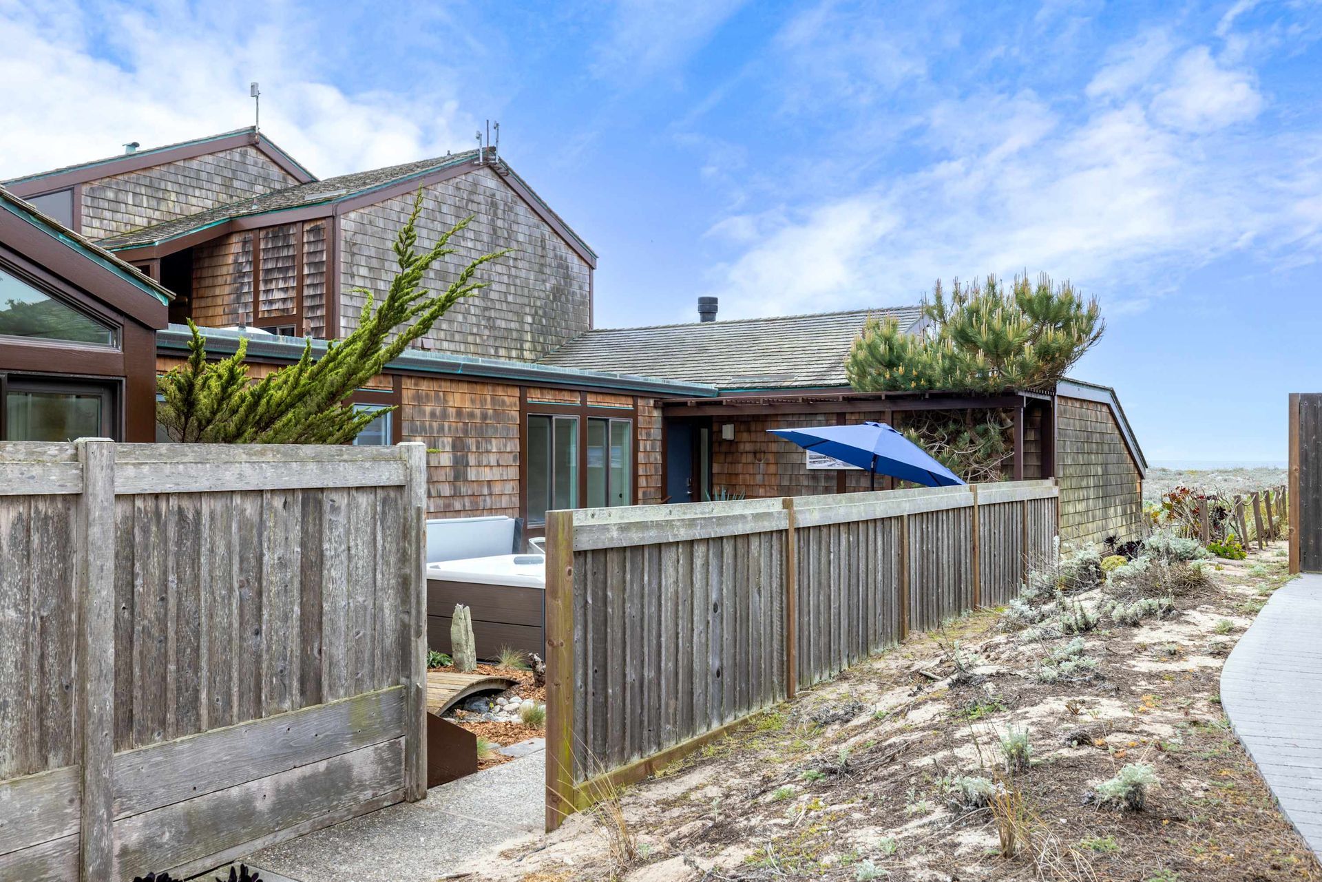 A wooden fence surrounds a house with a hot tub in the backyard.