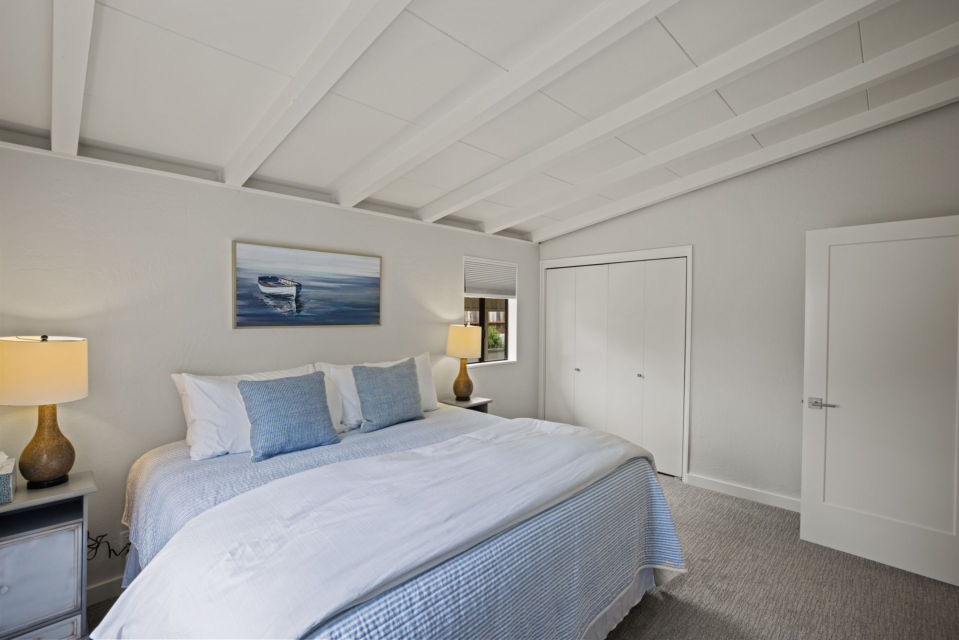 A bedroom with a bed , two lamps , and a painting on the wall.