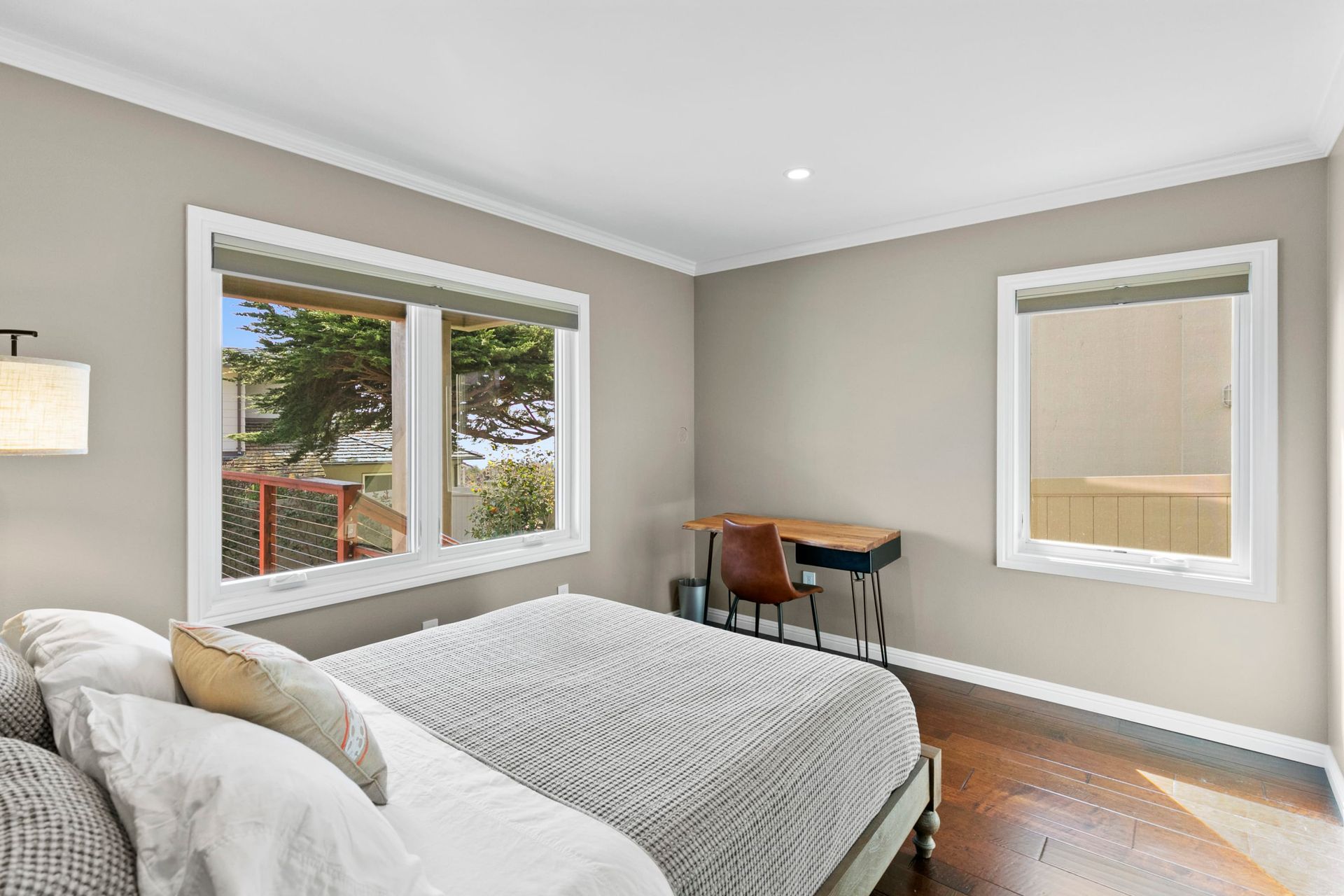 A bedroom with a bed , desk and two windows.