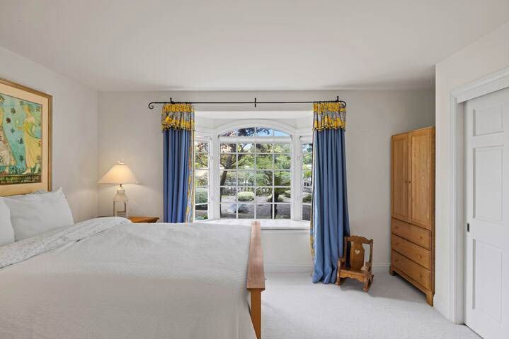 A bedroom with a bed , dresser , window and curtains.
