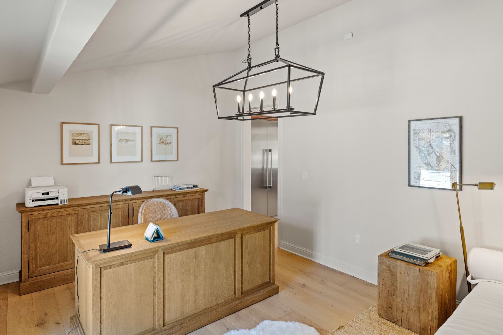 A home office with a wooden desk and a chandelier hanging from the ceiling.
