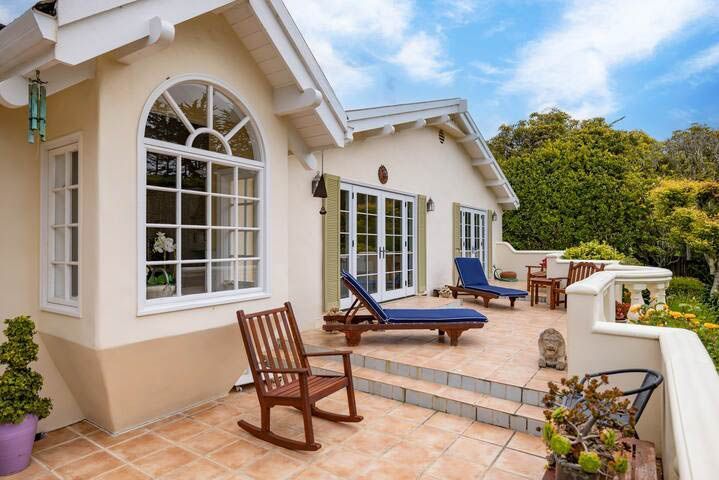 There are two rocking chairs on the patio in front of the house.