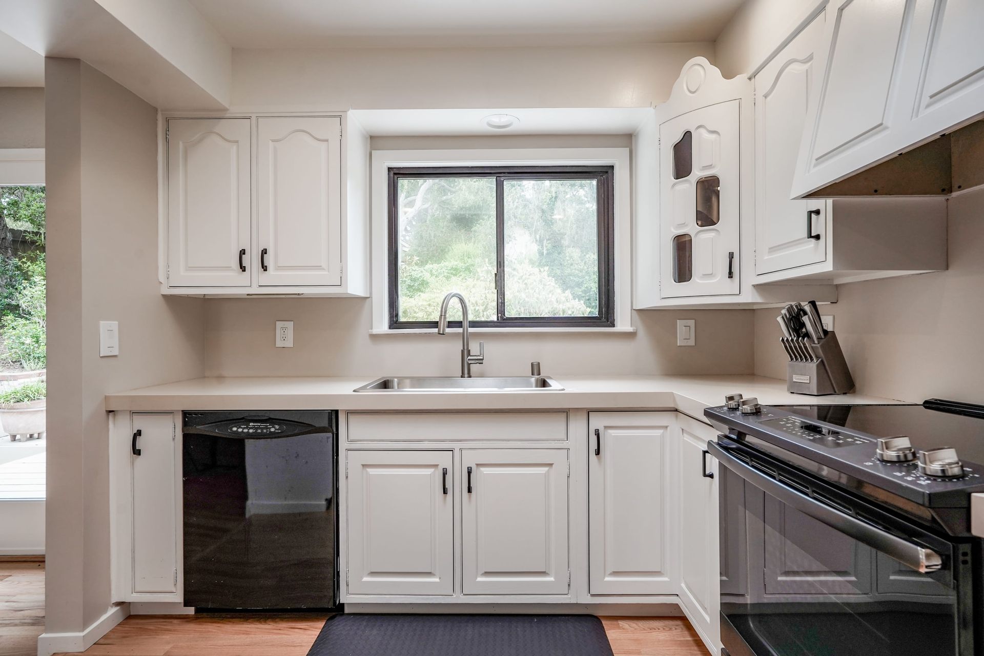 A kitchen with white cabinets , a stove , a sink , and a window.