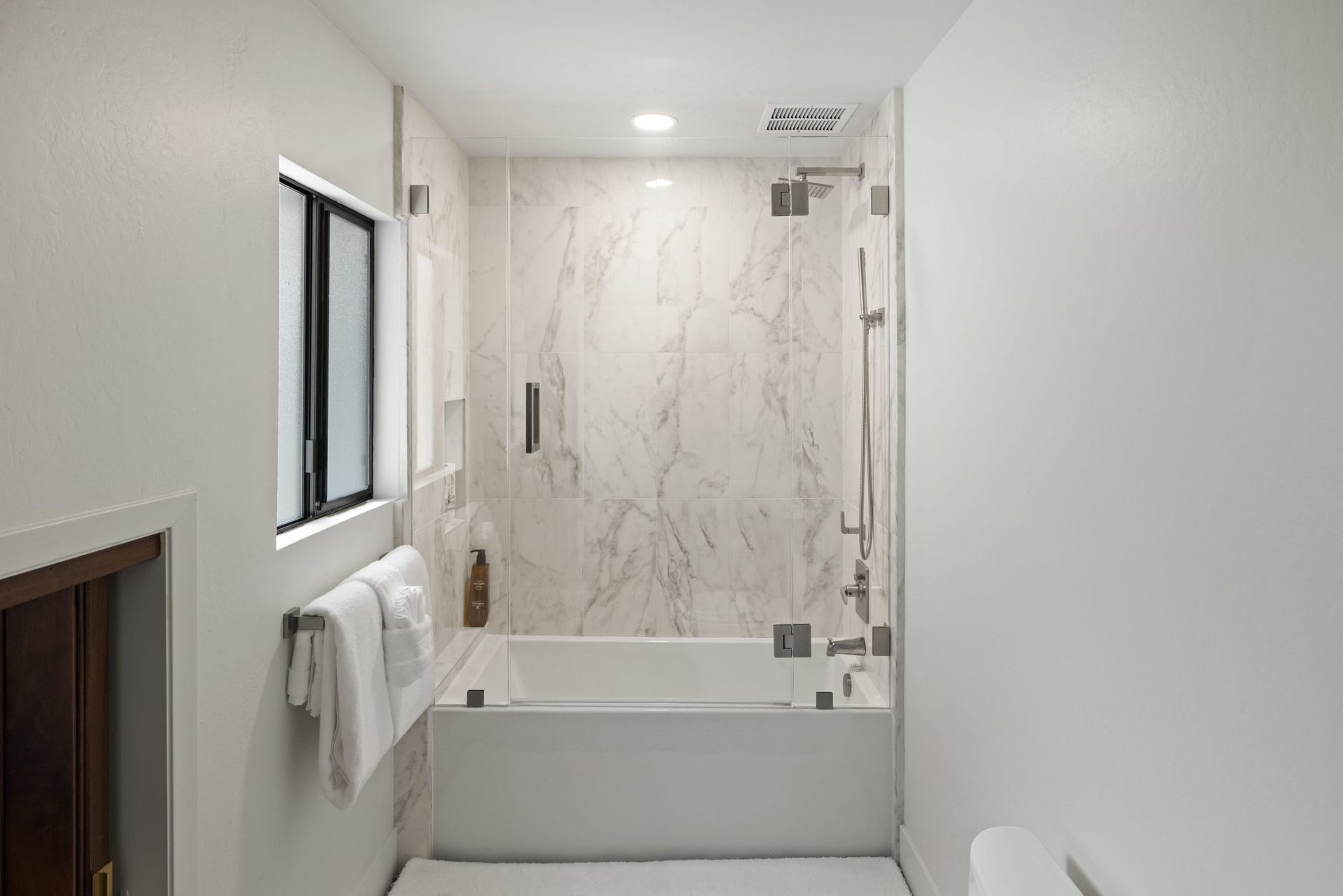 A bathroom with a tub , shower , toilet and window.