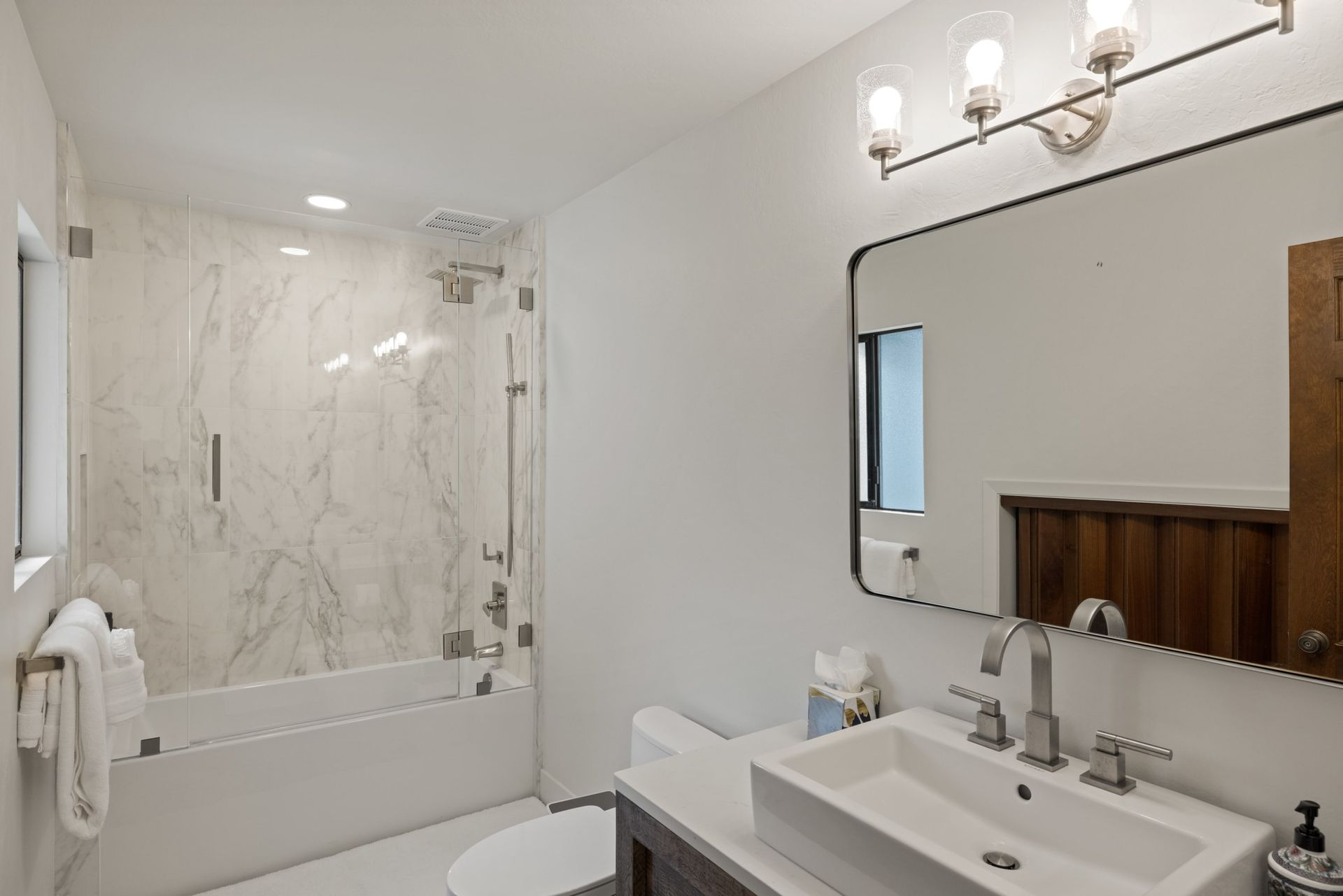 A bathroom with a sink , toilet , shower and mirror.