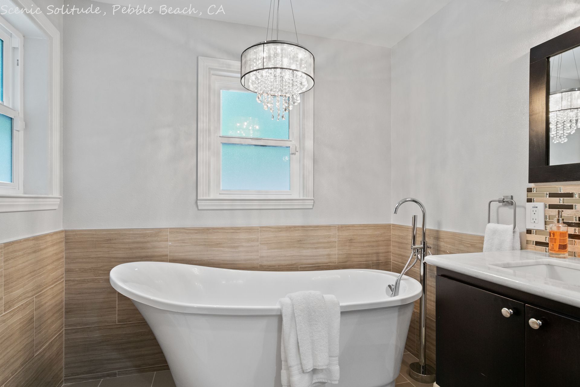 A bathroom with a tub , sink , mirror and window.