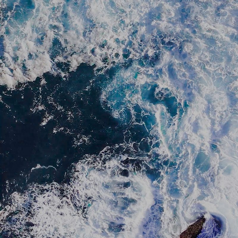 An aerial view of a large body of water with waves crashing against a rock.