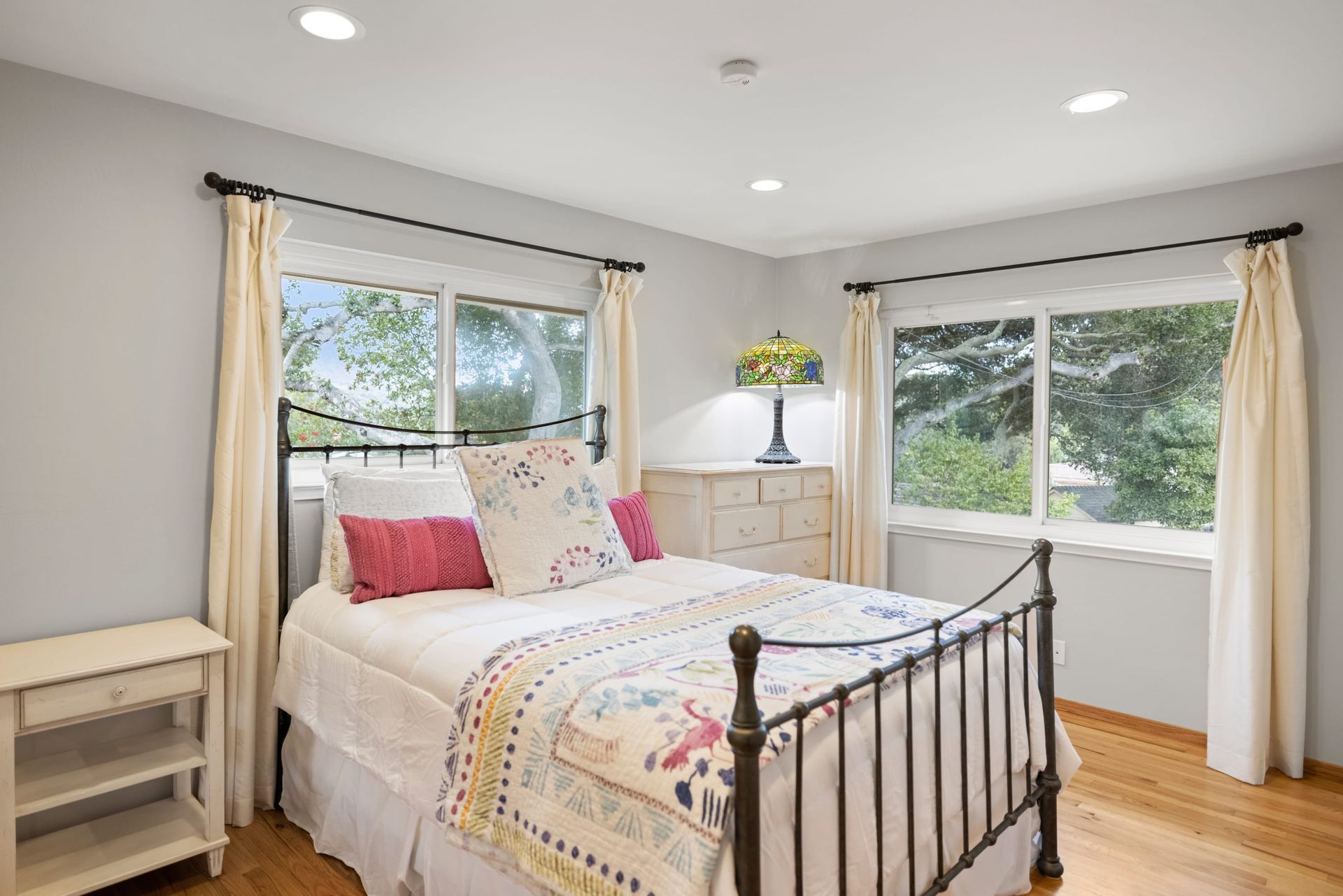 A bedroom with a bed , dresser , nightstand and two windows.